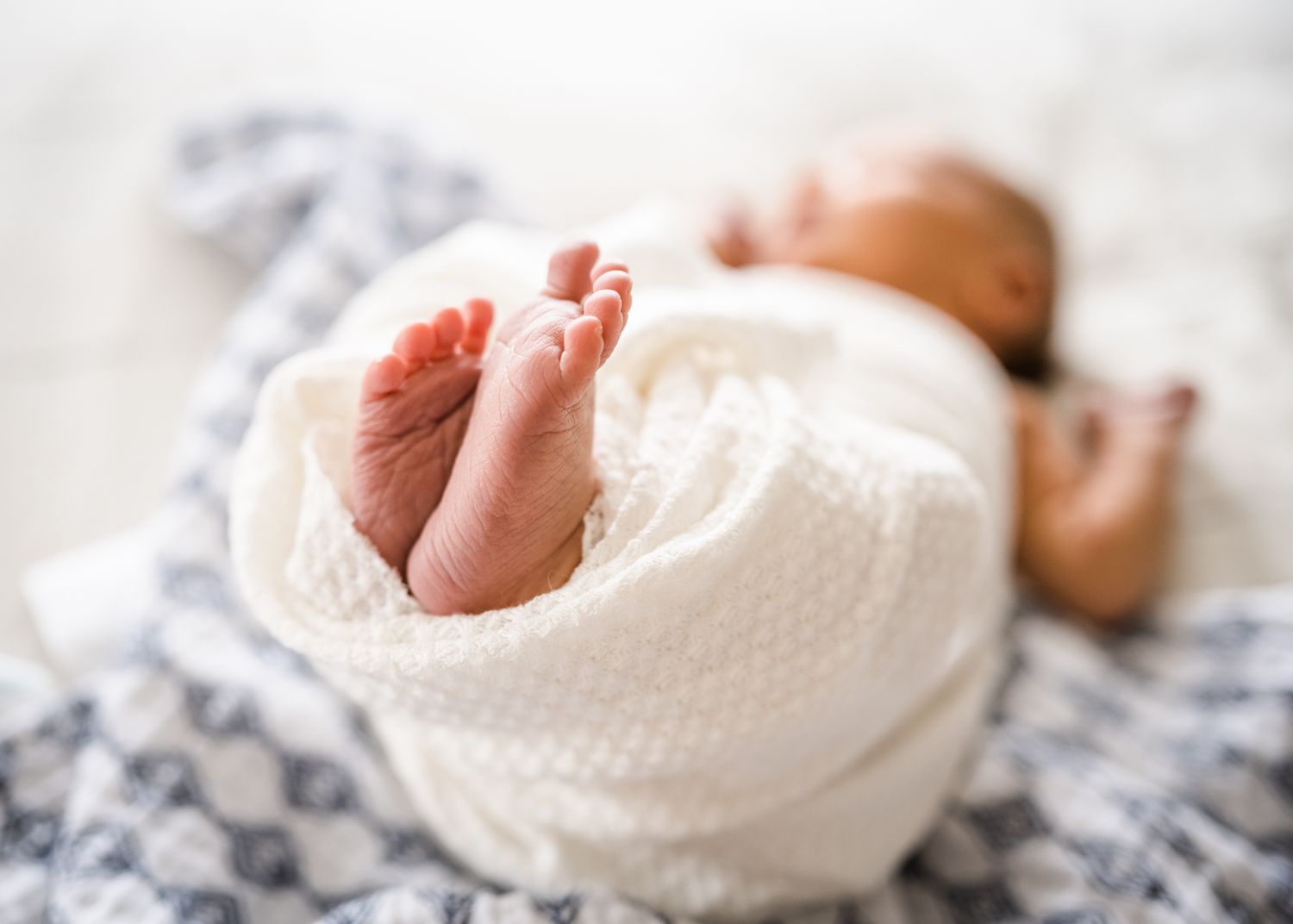 Newborn's tiny feet peeking out from white knit blanket.