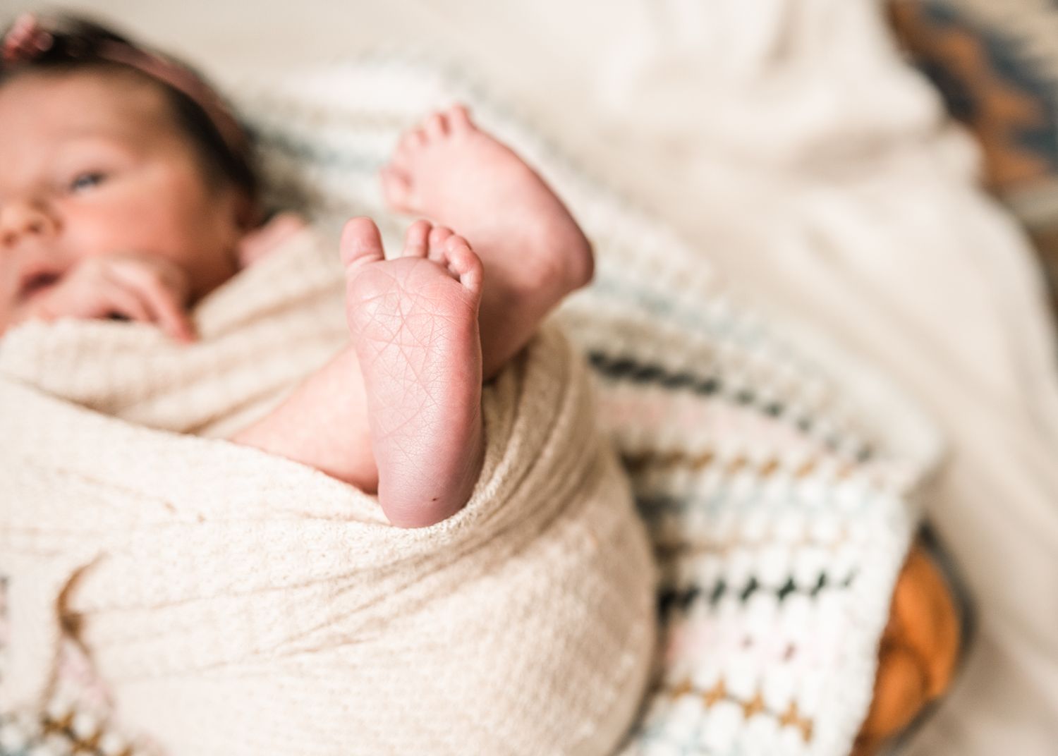 Close-up of newborn baby's tiny foot wrapped in soft beige blanket.