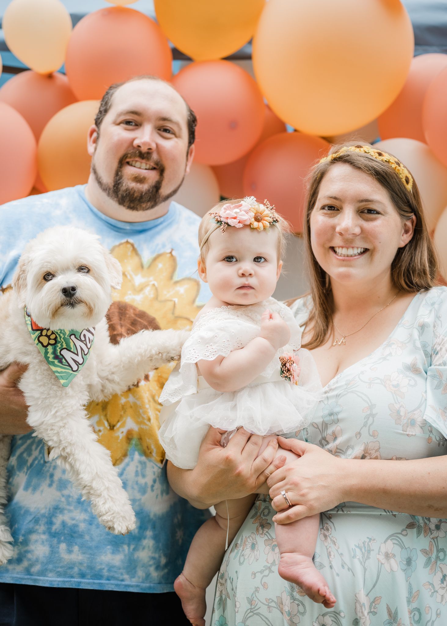 Family portrait with white dog against peachy balloon backdrop.