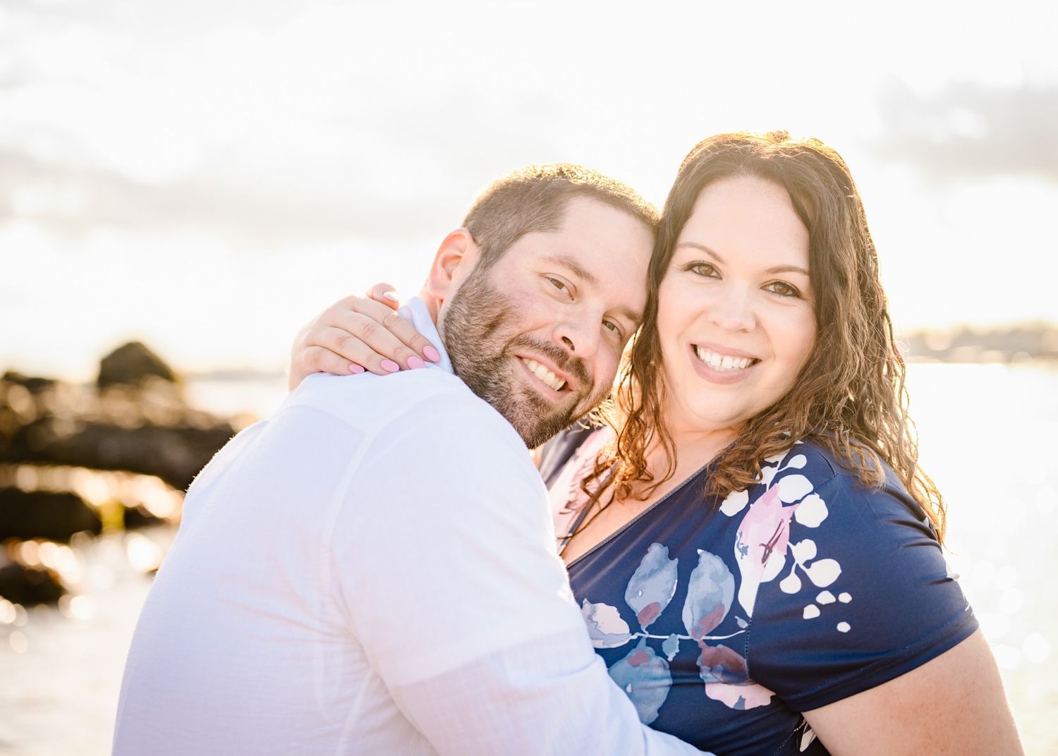 A joyful couple embraces and laughs together on a sunny beach.