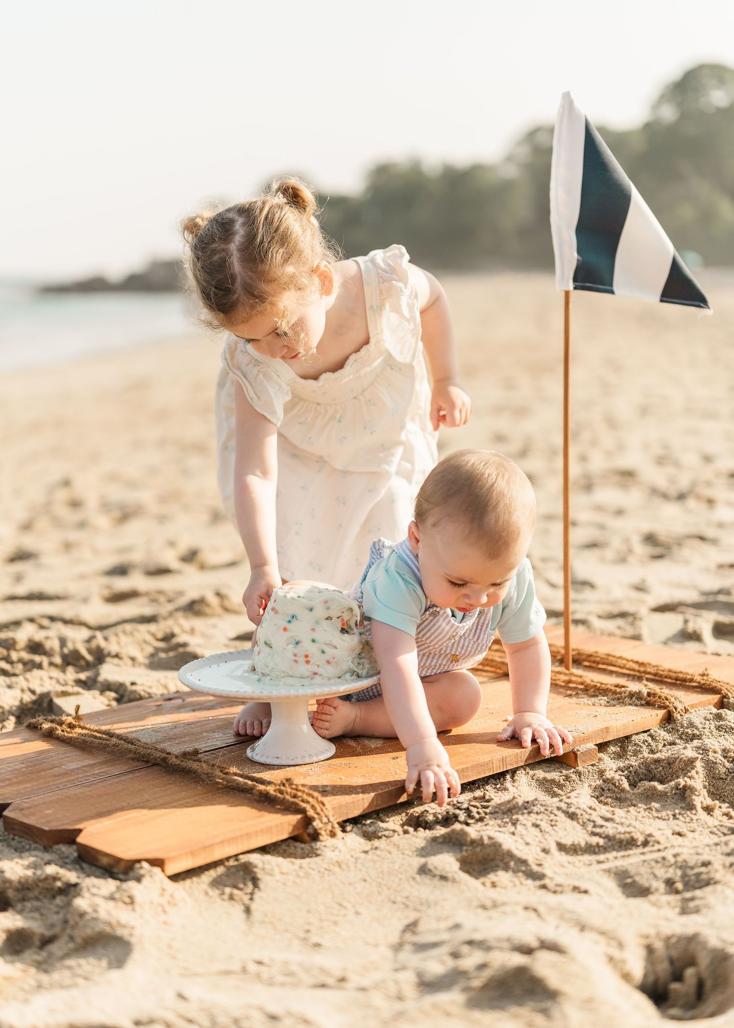 Children drawing with chalk on wooden boards while sitting on a sandy beach at sunset.