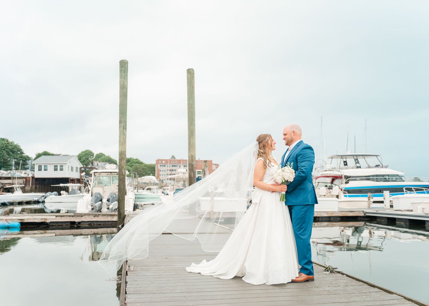Newly married couple standing on a wooden dock surrounded by boats at a marina.