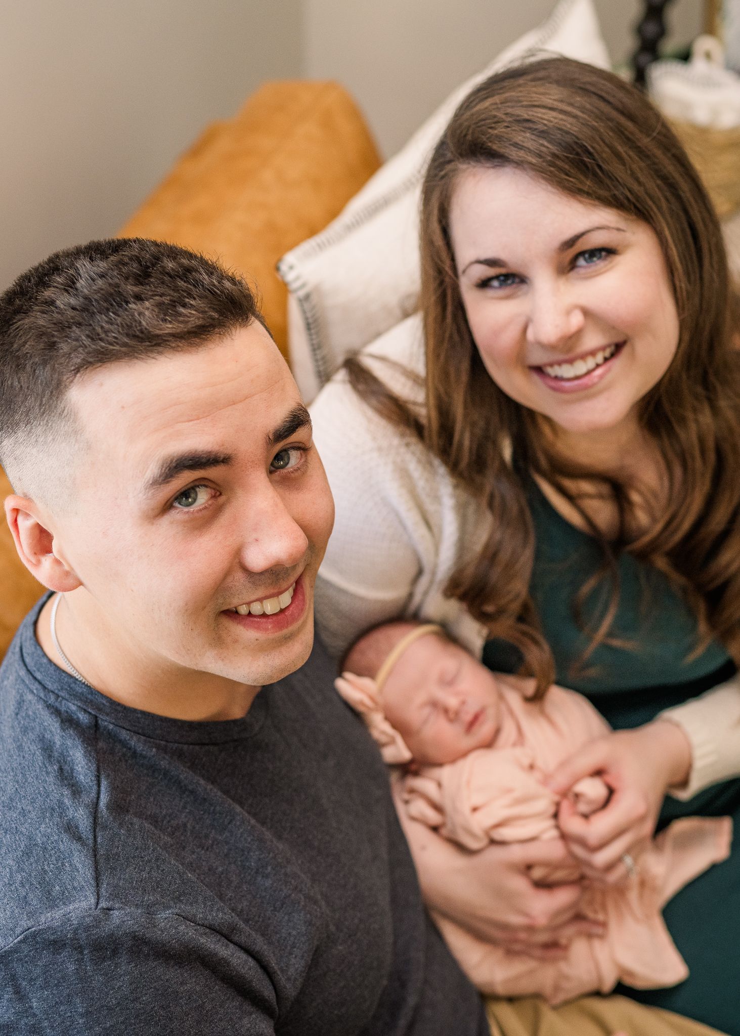 A cozy family moment on a brown couch with a small baby in pink.