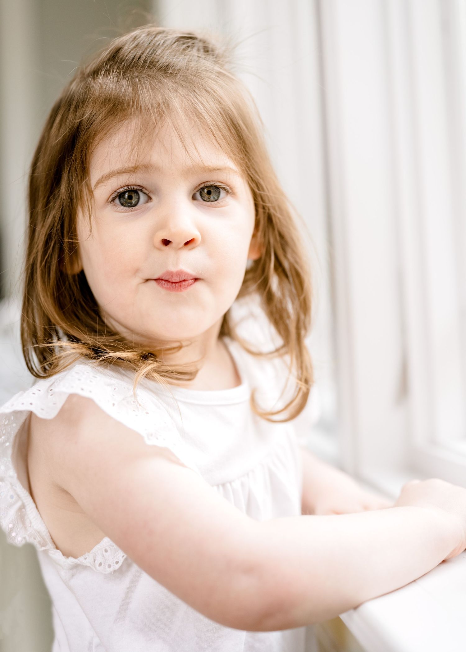A sweet portrait of a young child with shoulder-length hair wearing a white dress.