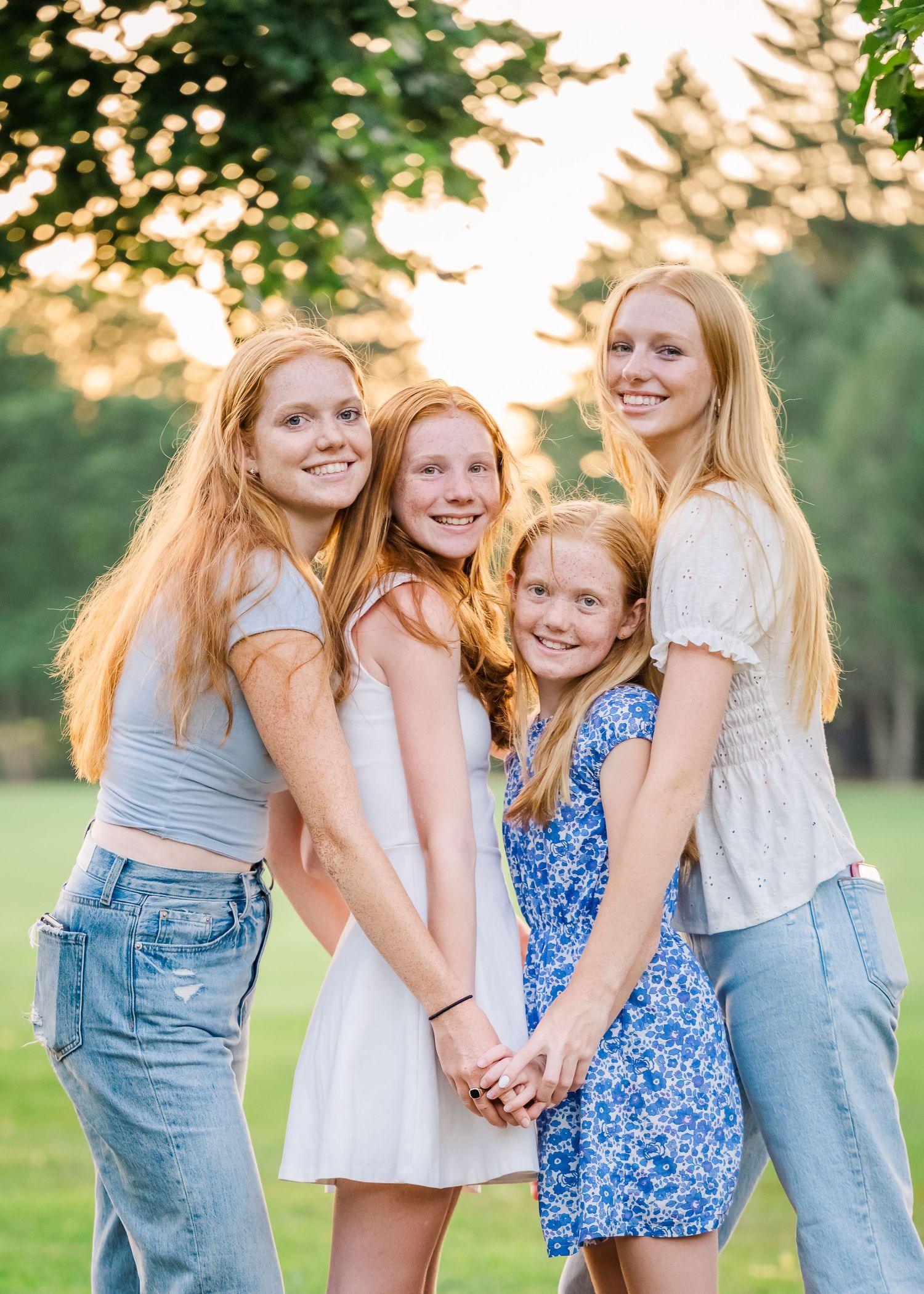Four siblings hold hands in a circle while posing for a sunset portrait outdoors.