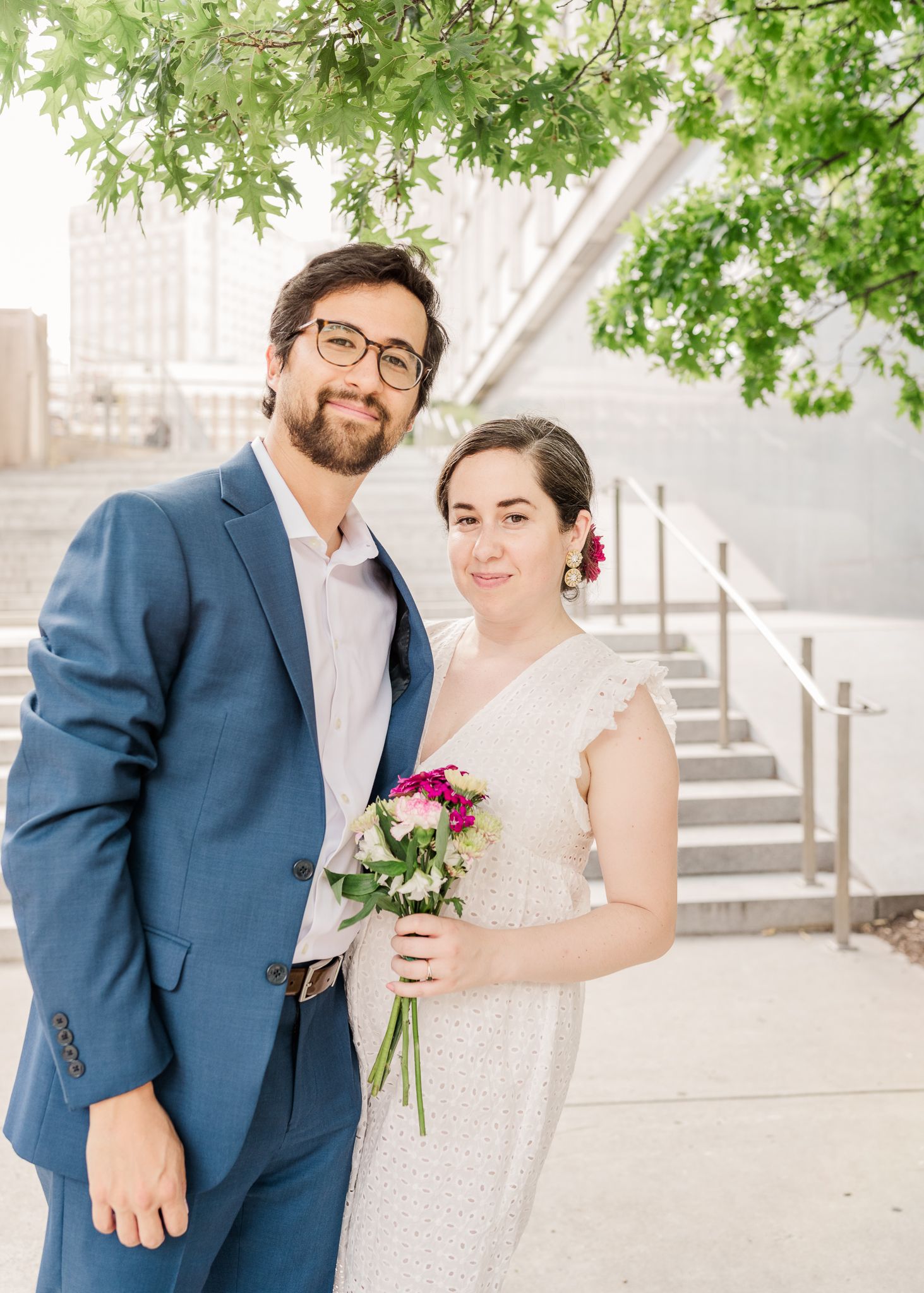 Elegant couple portrait with spring foliage and urban architecture in background.