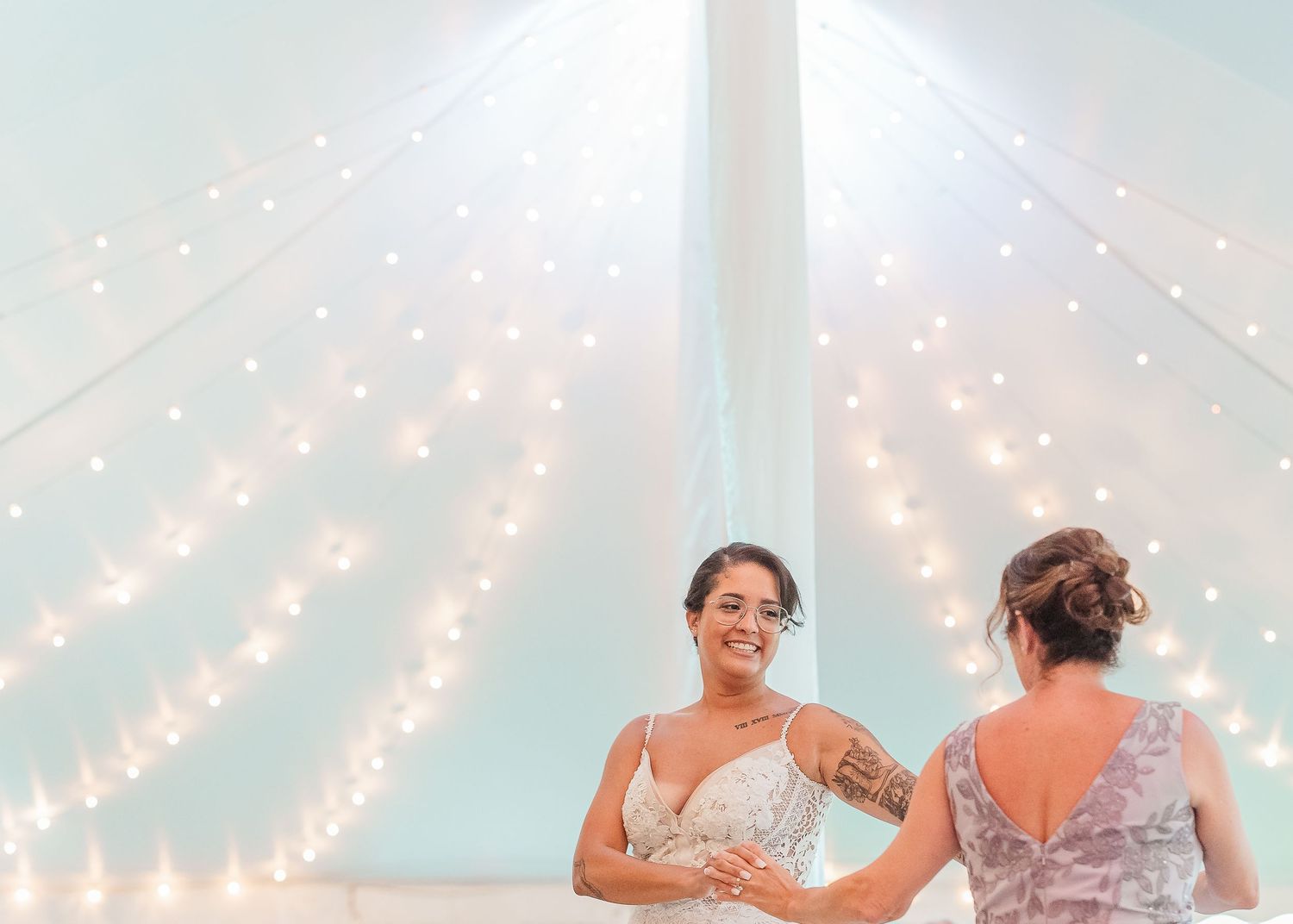 A couple dances in an intimate moment under warm string lights at a romantic outdoor celebration.