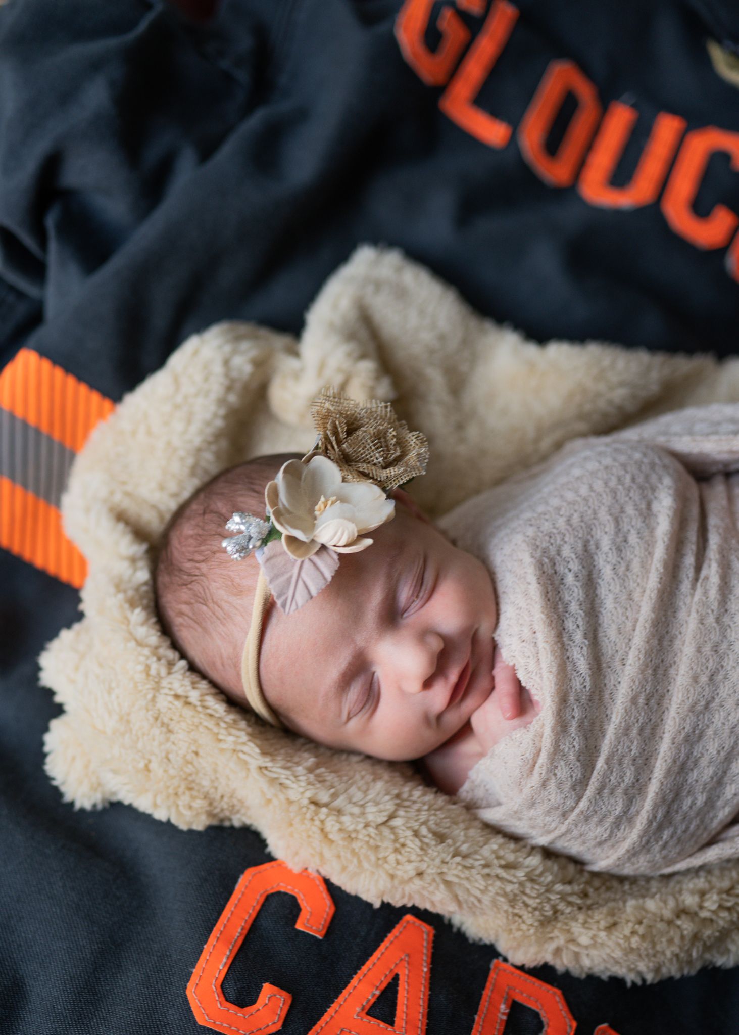 Sleeping newborn wrapped in gray swaddle on sherpa blanket with orange lettering.