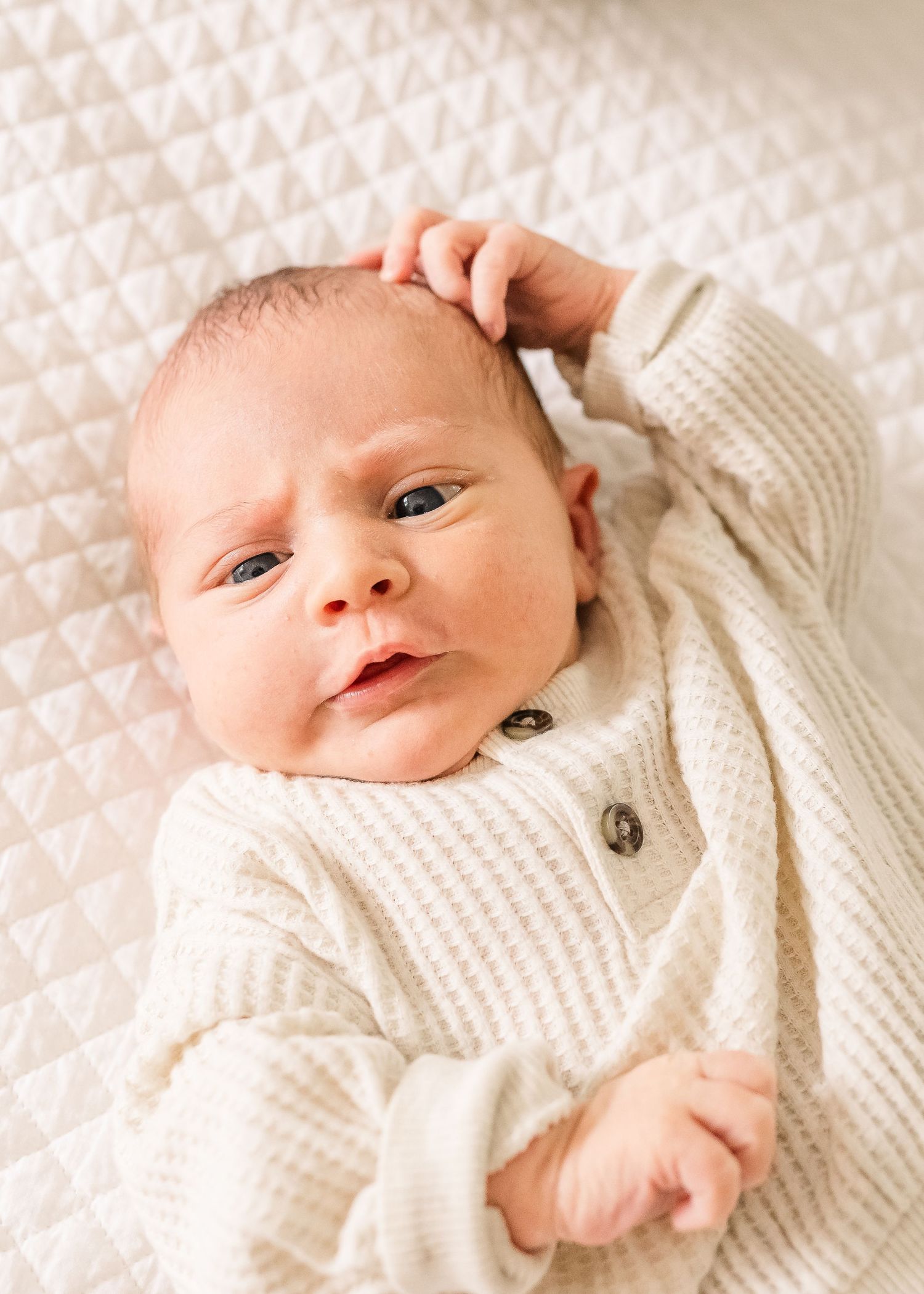 Newborn baby wearing white knit cardigan looking directly at camera.