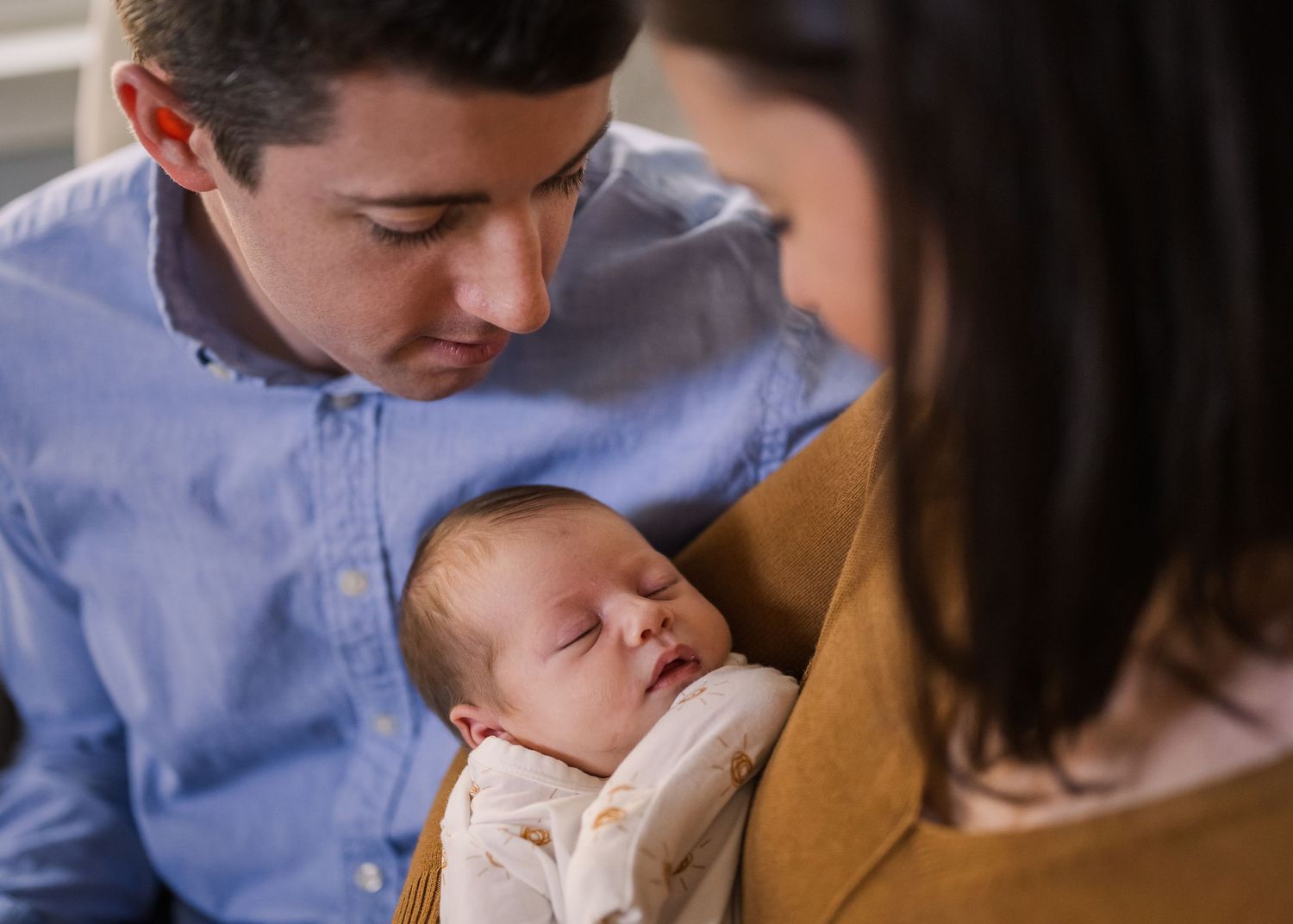 An intimate moment between parents and their sleeping newborn in white onesie.