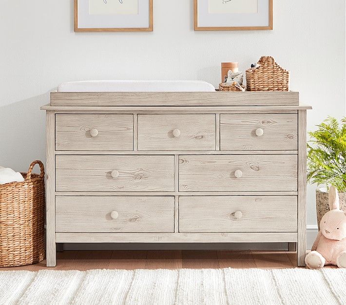 Light gray wooden dresser with seven drawers and changing table top for nursery storage.