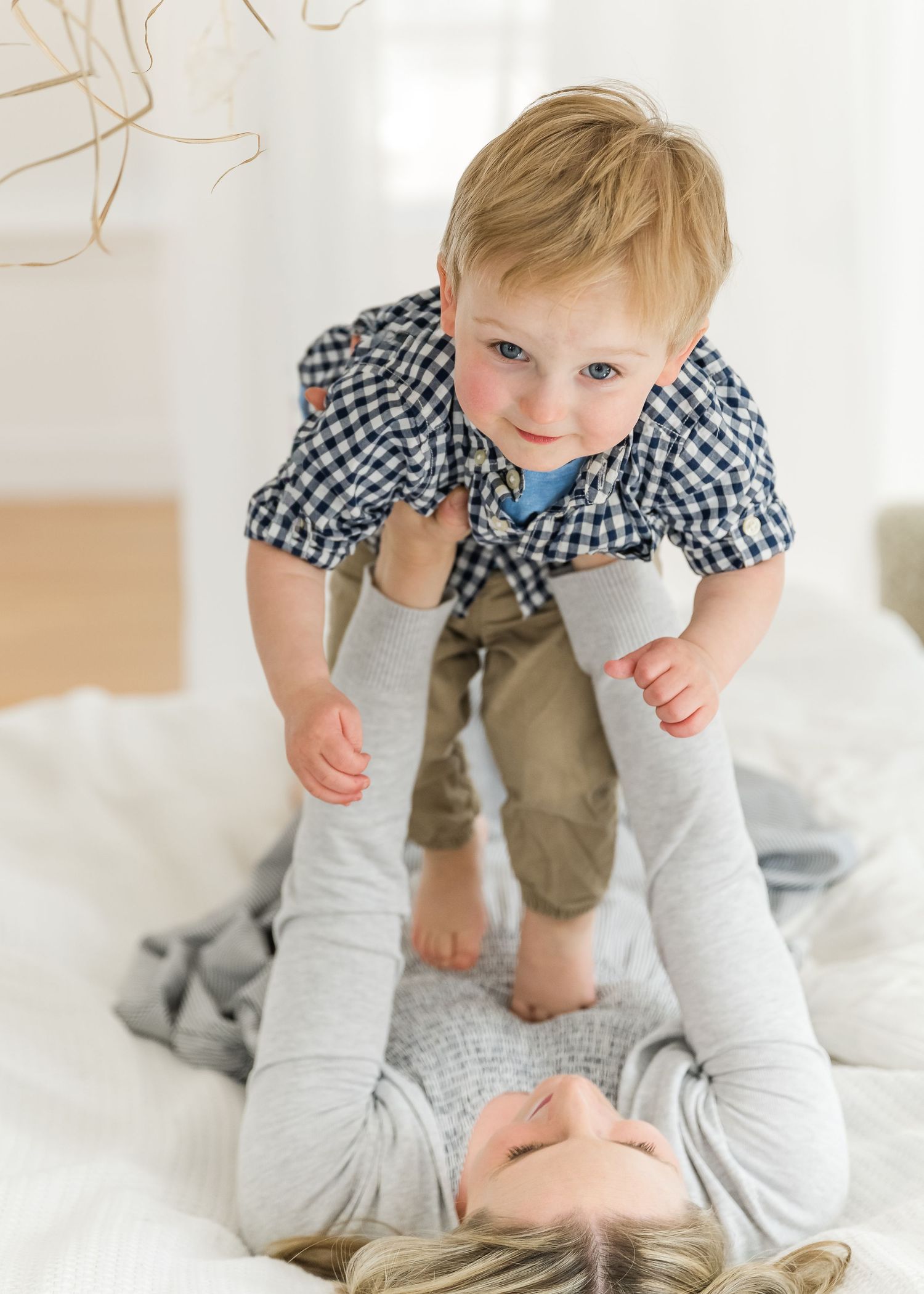 An intimate moment of playtime on a white bed with a small child being lifted up by someone lying down.