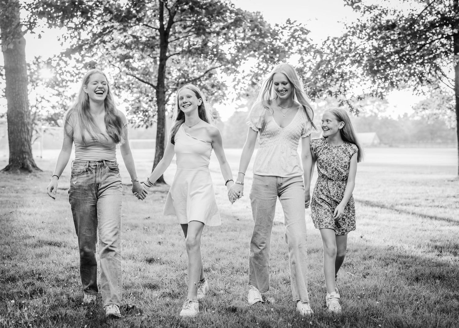 Black and white photo of four people walking hand in hand through a grassy field.