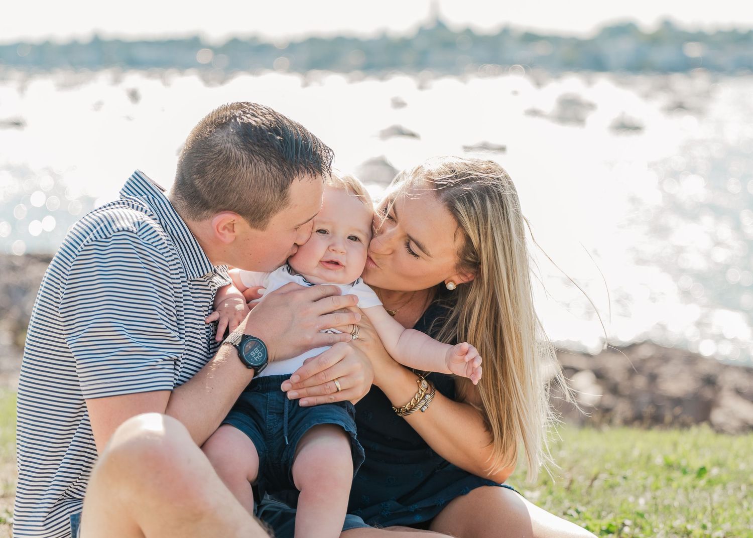 A loving family shares a tender moment together while sitting outdoors near the ocean on a sunny day.