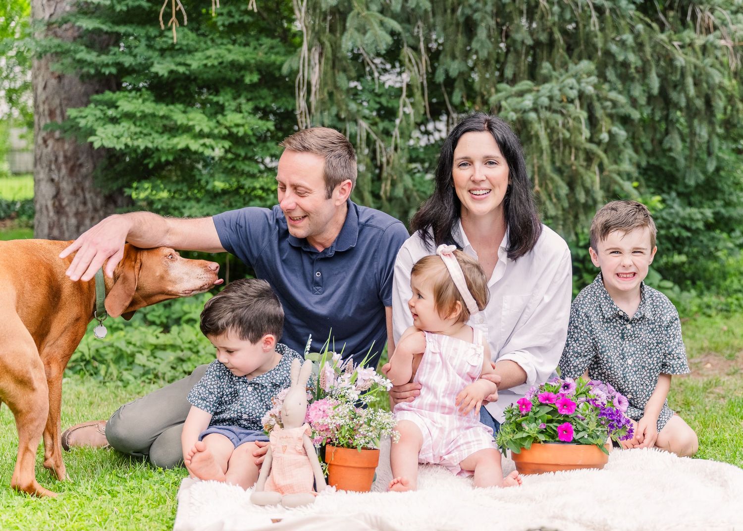 Outdoor family gathering with pet dog and potted flowers on blanket.
