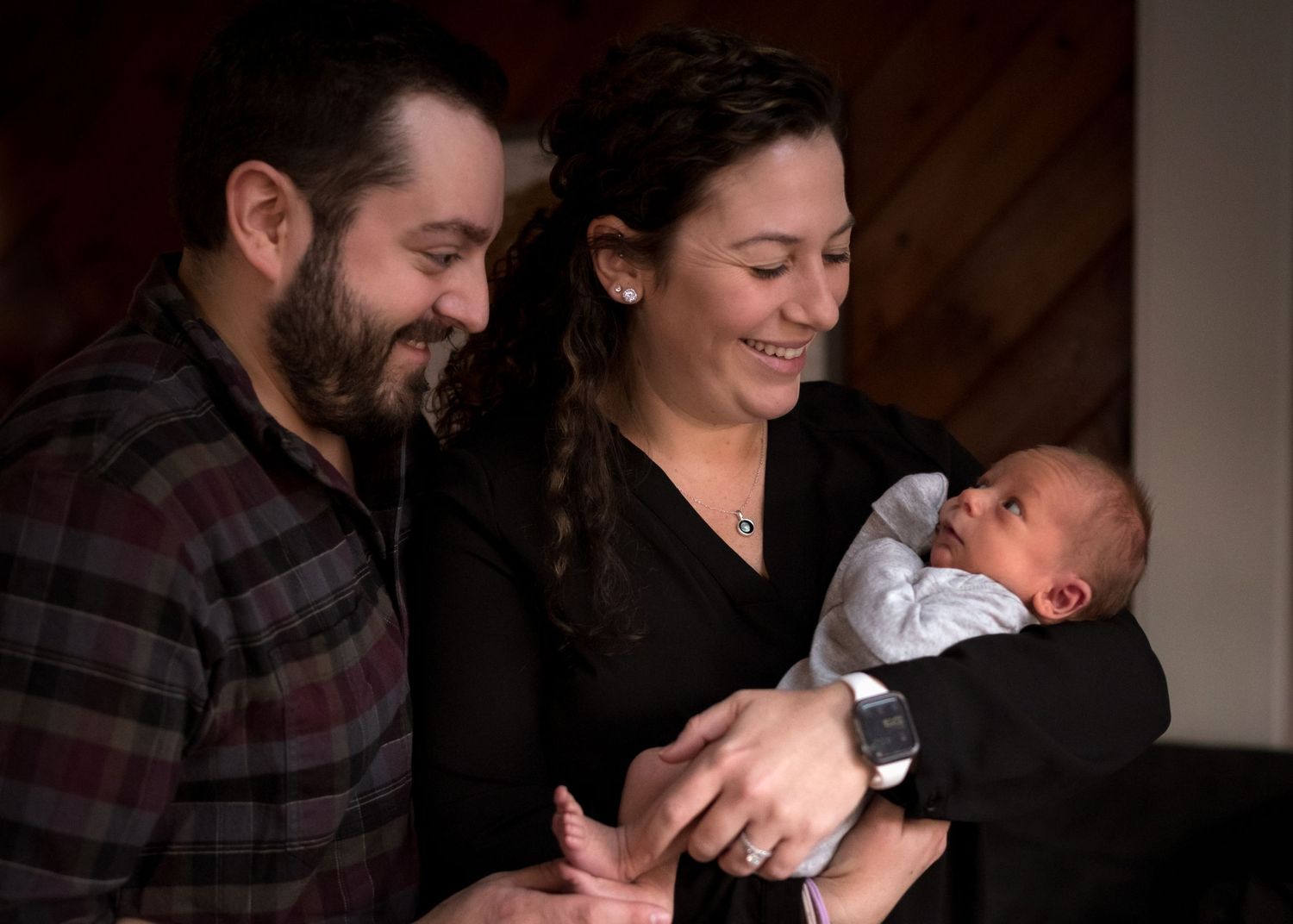 Parents sharing intimate moment with newborn baby in warm indoor lighting.