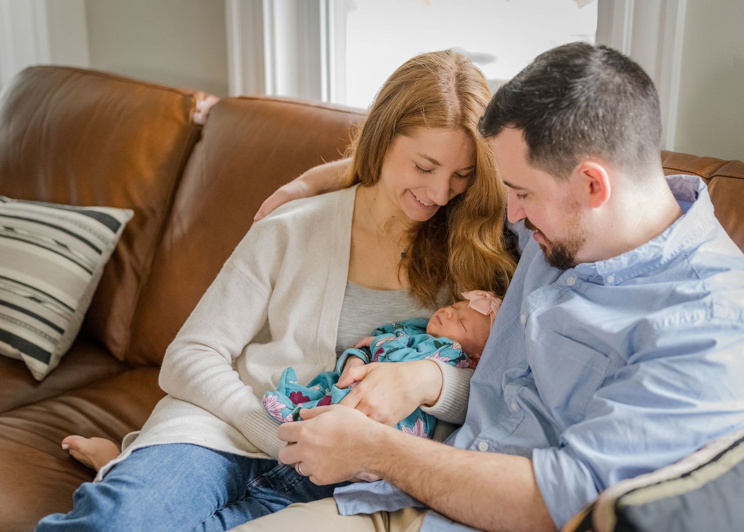 Family sharing tender moment with newborn on leather sectional.