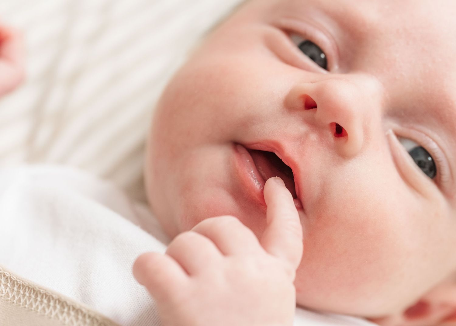Close-up portrait of a baby with rosy cheeks lying on white bedding.
