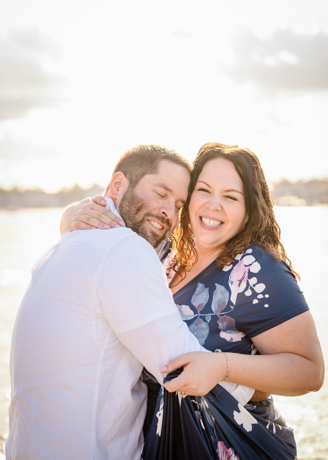 A couple shares laughter while embracing on a bright coastal beach.