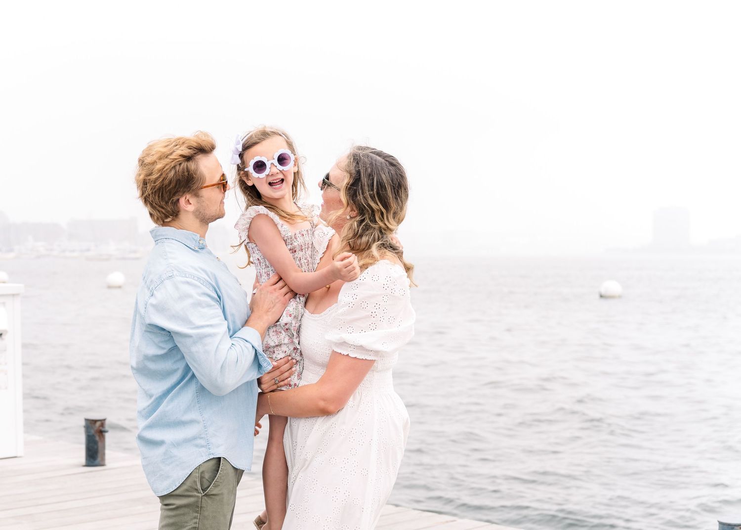 A joyful family portrait on a waterfront dock showing playful interaction and laughter.