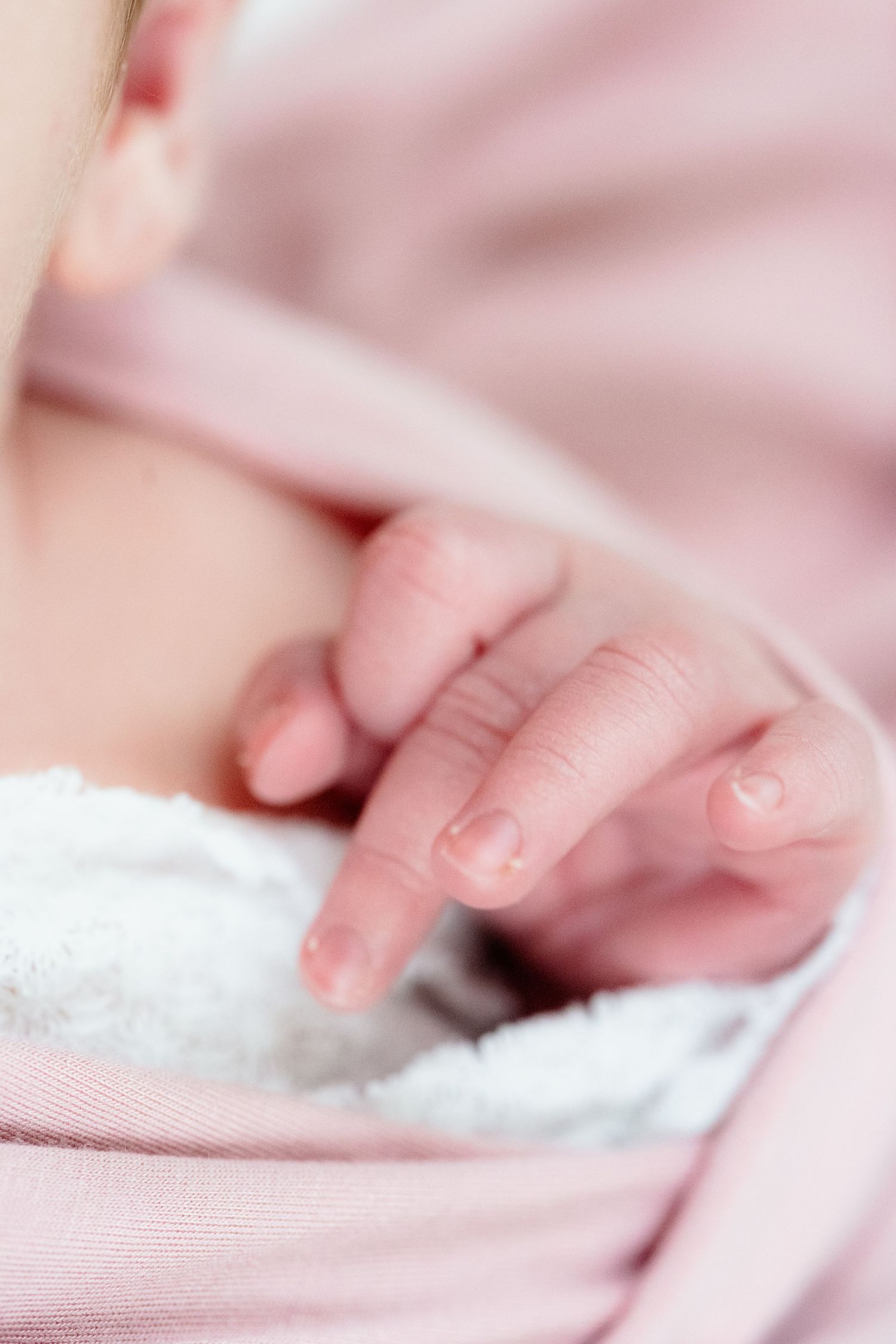 A tiny newborn baby's hand with delicate pink fingers grasps onto a white blanket.