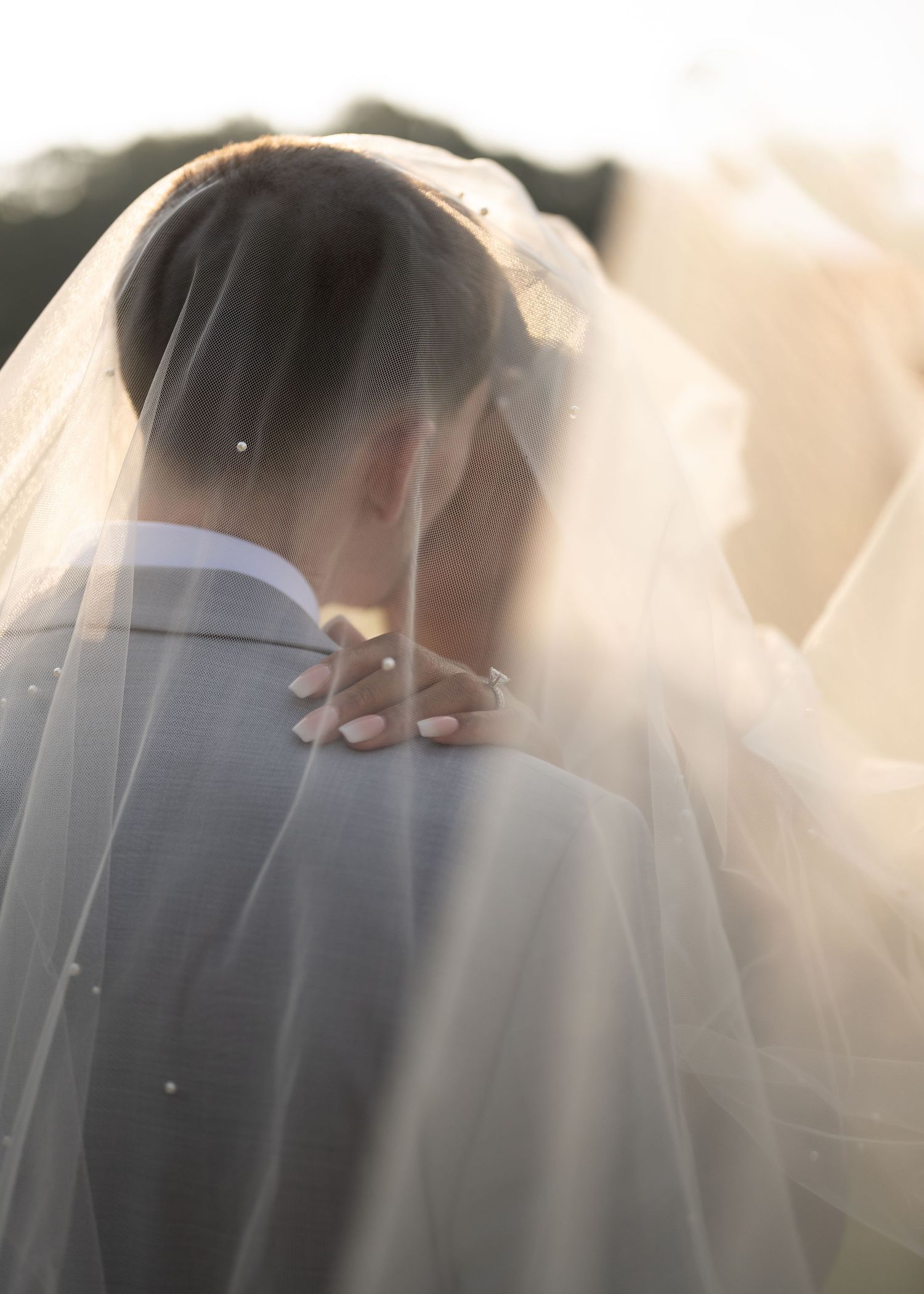 A tender moment between a couple on their wedding day with the bride's veil flowing in soft light.