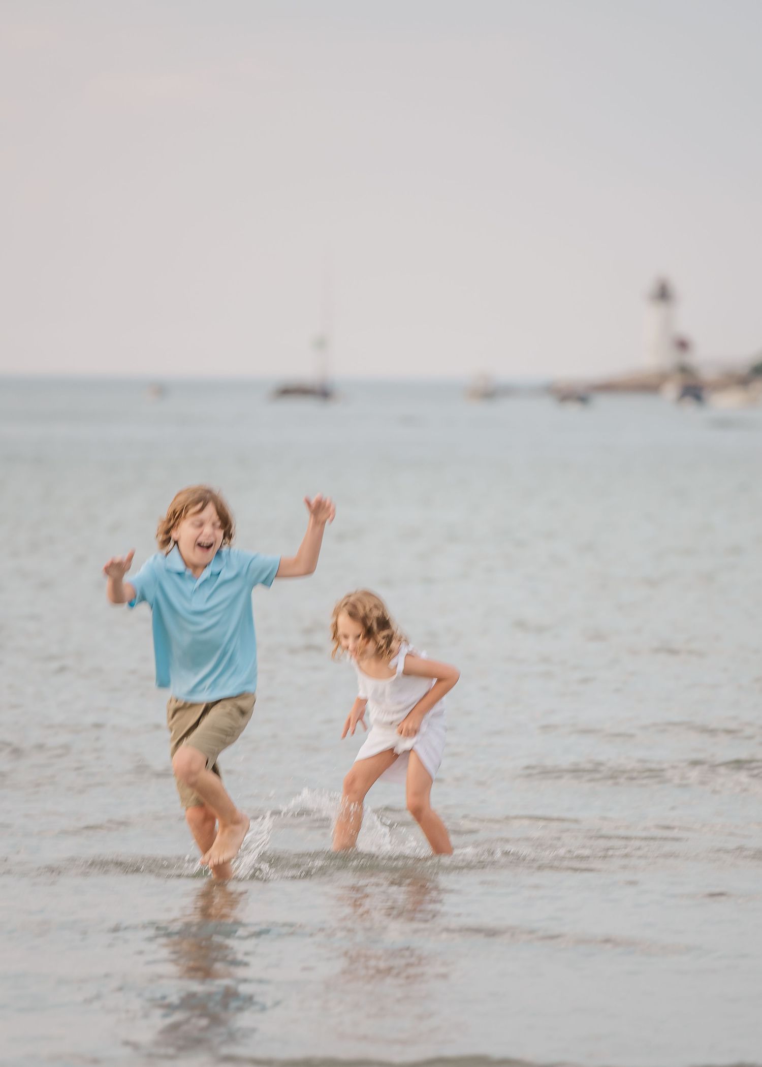 Children splashing and playing in shallow ocean water at sunset.