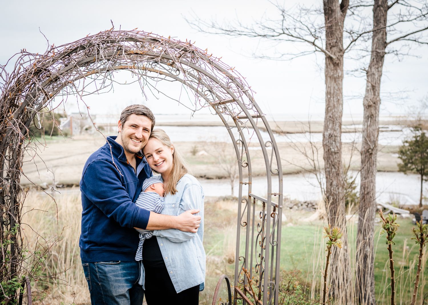 A couple embracing under a decorative garden arch with natural landscape in the background.