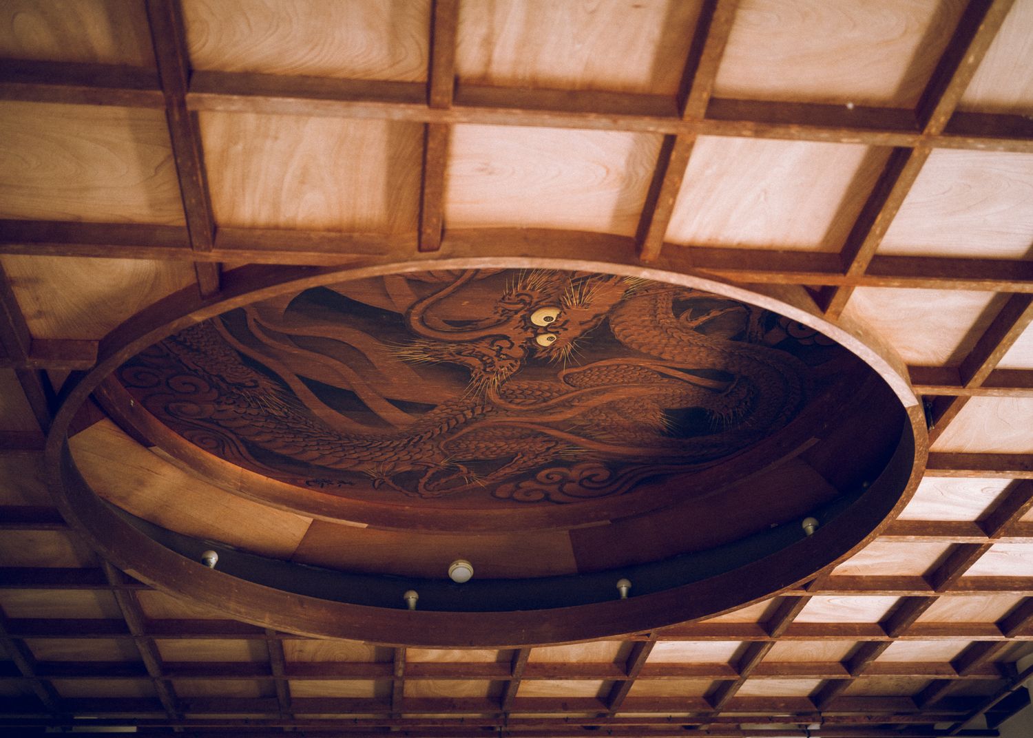 Ornate wooden ceiling panel with carved dragon design in traditional Japanese architecture.