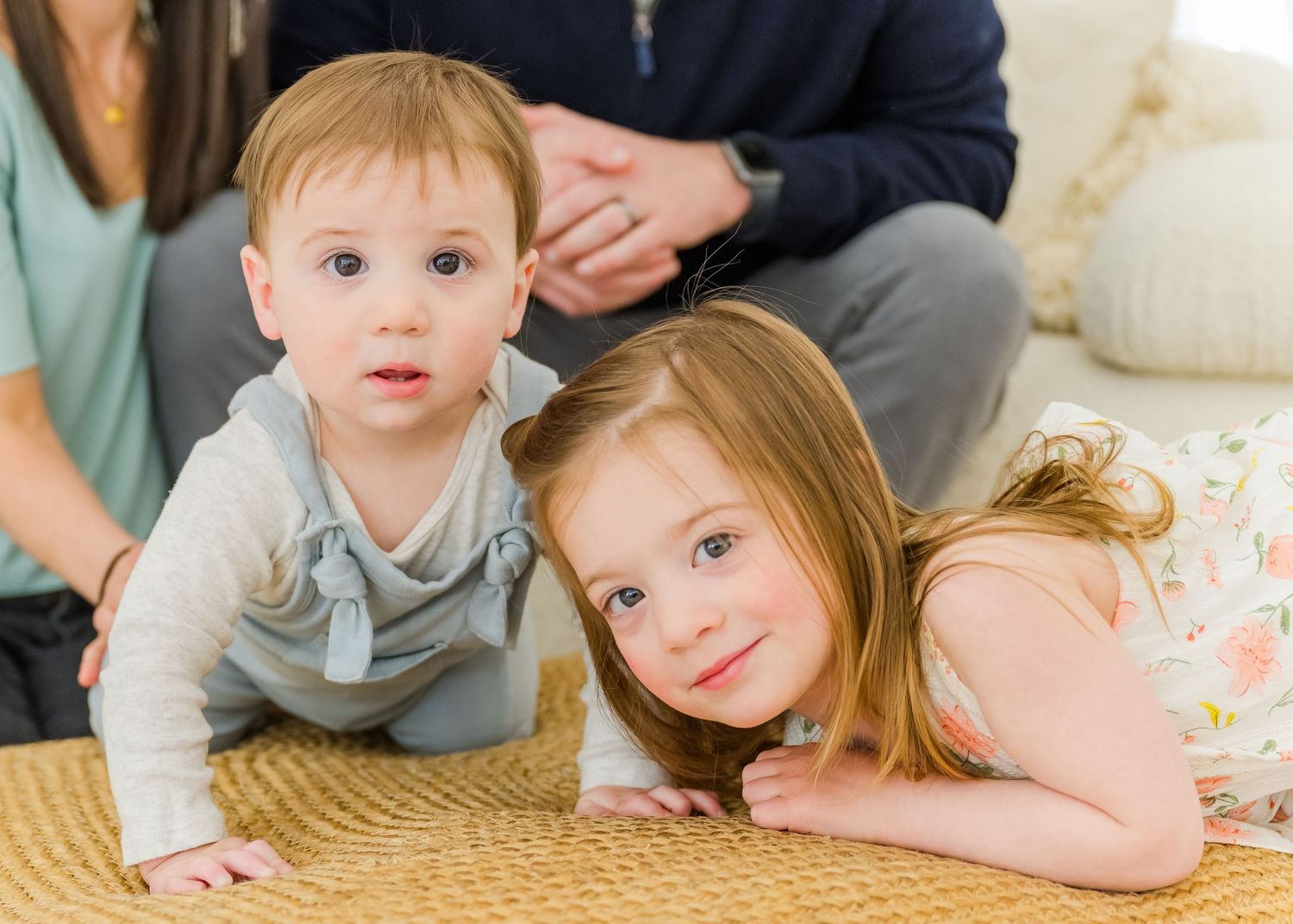 Two young children laying on a beige carpet while playing together indoors.