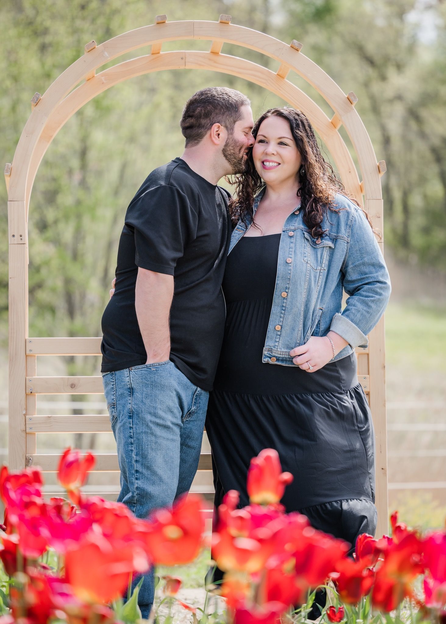 Intimate moment between couple under wooden arch with red tulips blooming below.