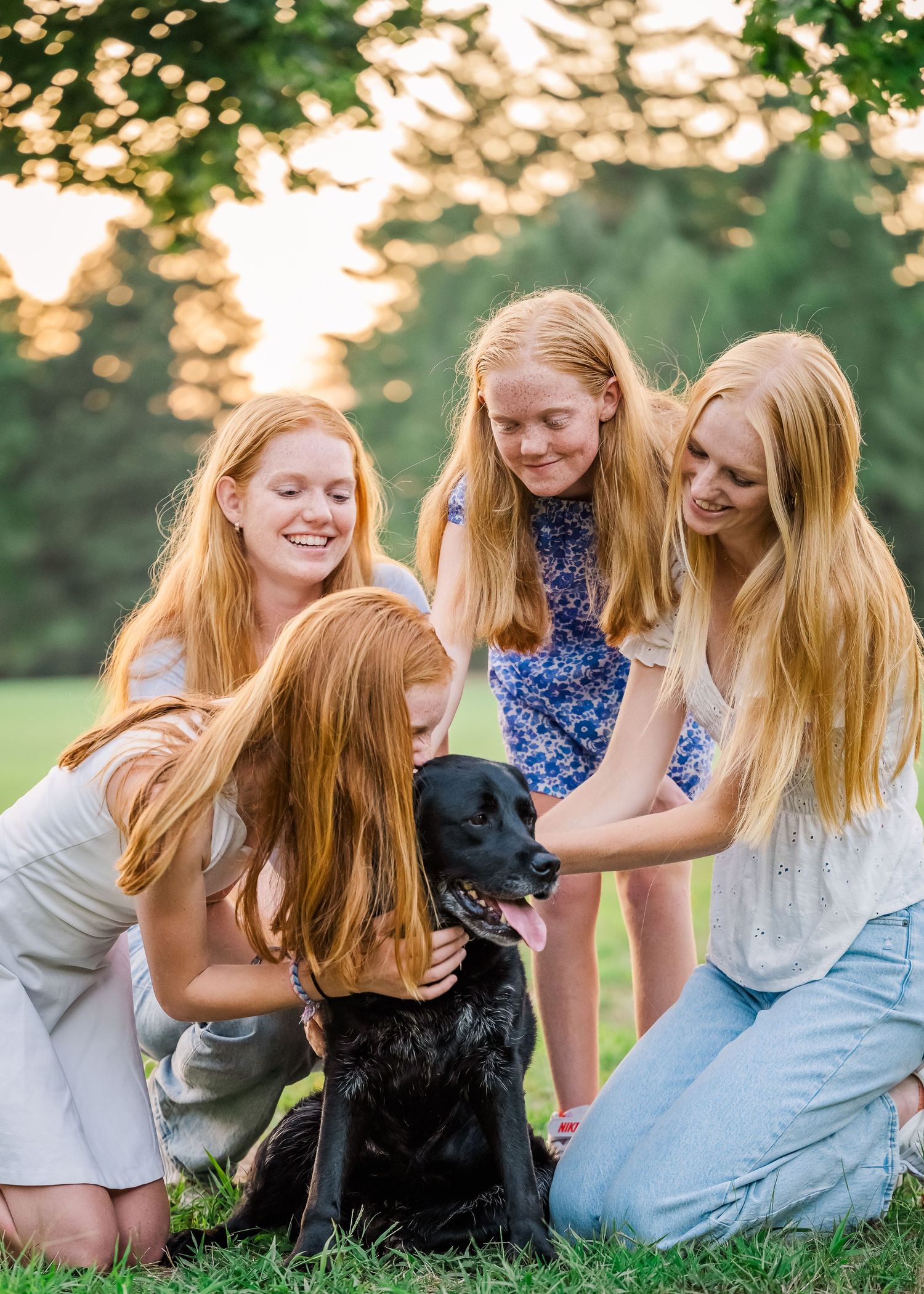 Group gathers around to pet and show affection to their black Labrador during an outdoor photoshoot.