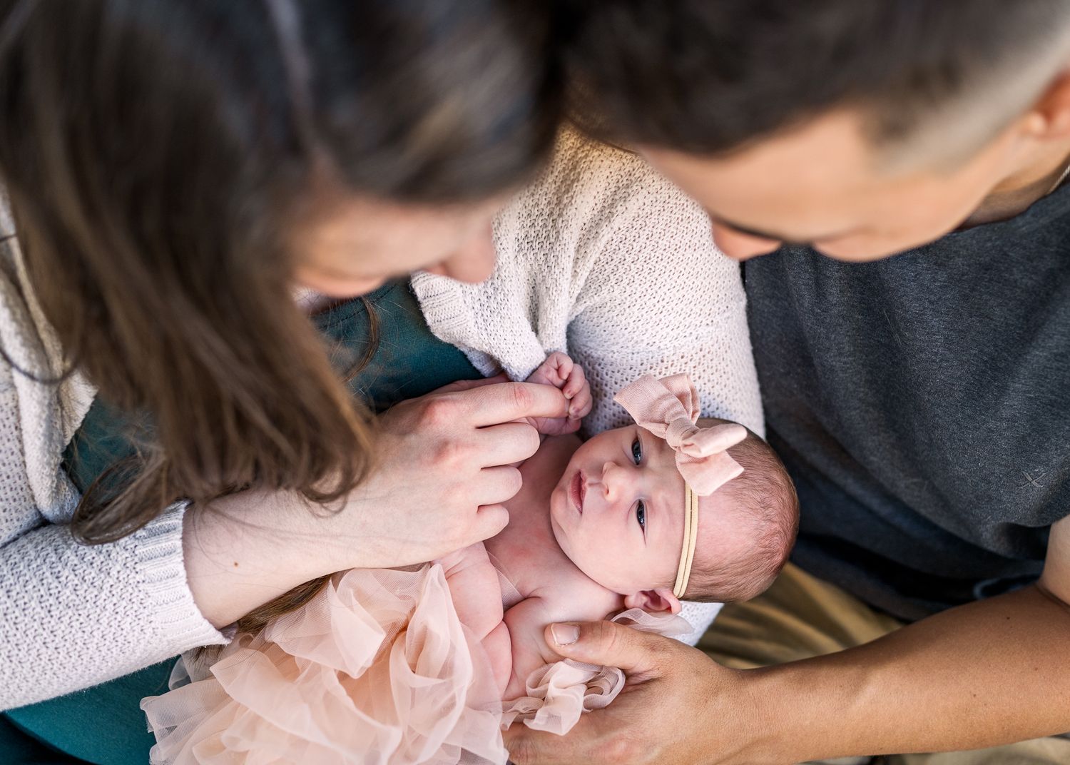 Tender moment with parents comforting newborn baby wrapped in pink.