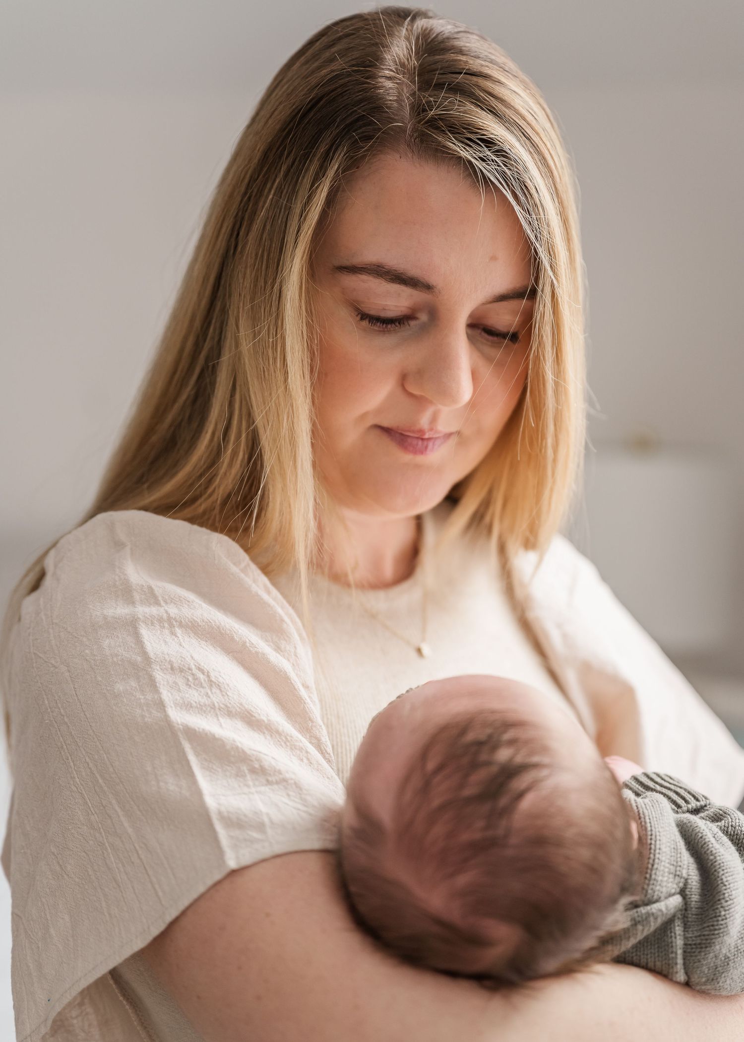 A tender moment captured as a mother in white holds and gazes lovingly at her newborn baby in natural light.