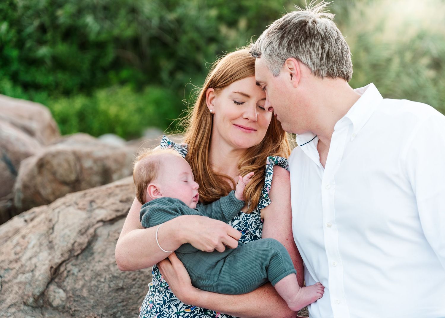 Happy family moment outdoors showing tender affection while holding a baby against a natural rocky background.
