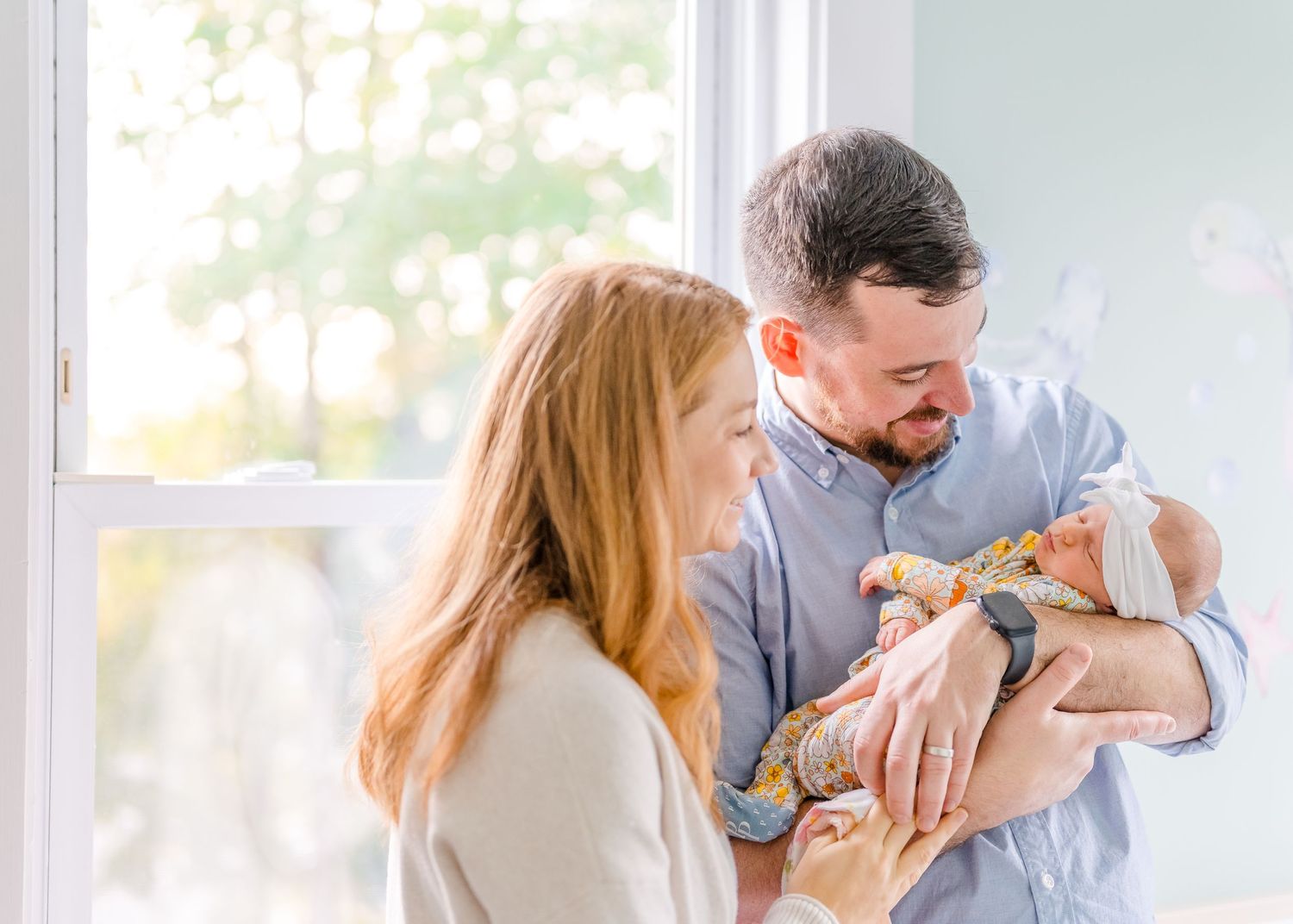 Parents gazing lovingly at their newborn baby by a sunny window.