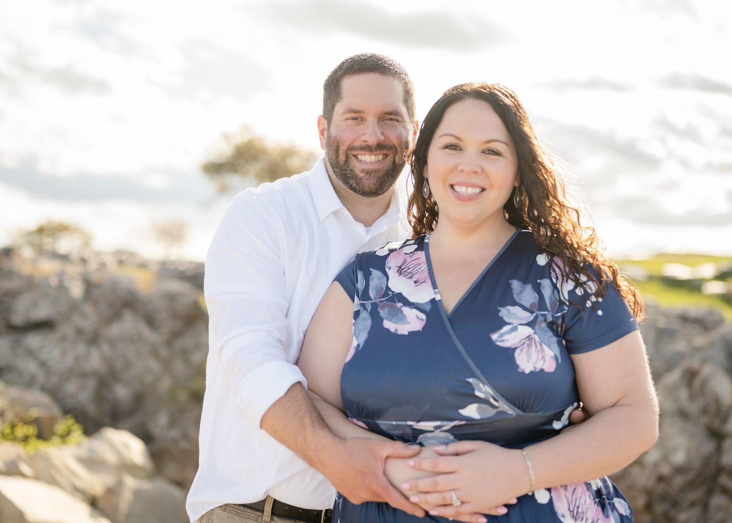 Couple poses together against rocky coastal backdrop during golden hour photo session.