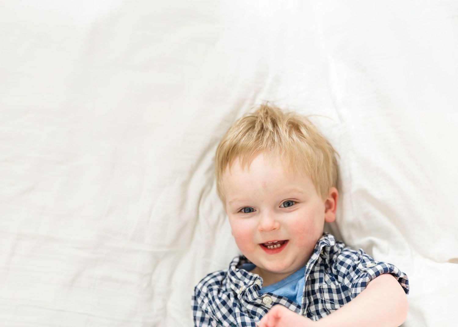A child wearing a blue and white checkered shirt smiles brightly against a light background.