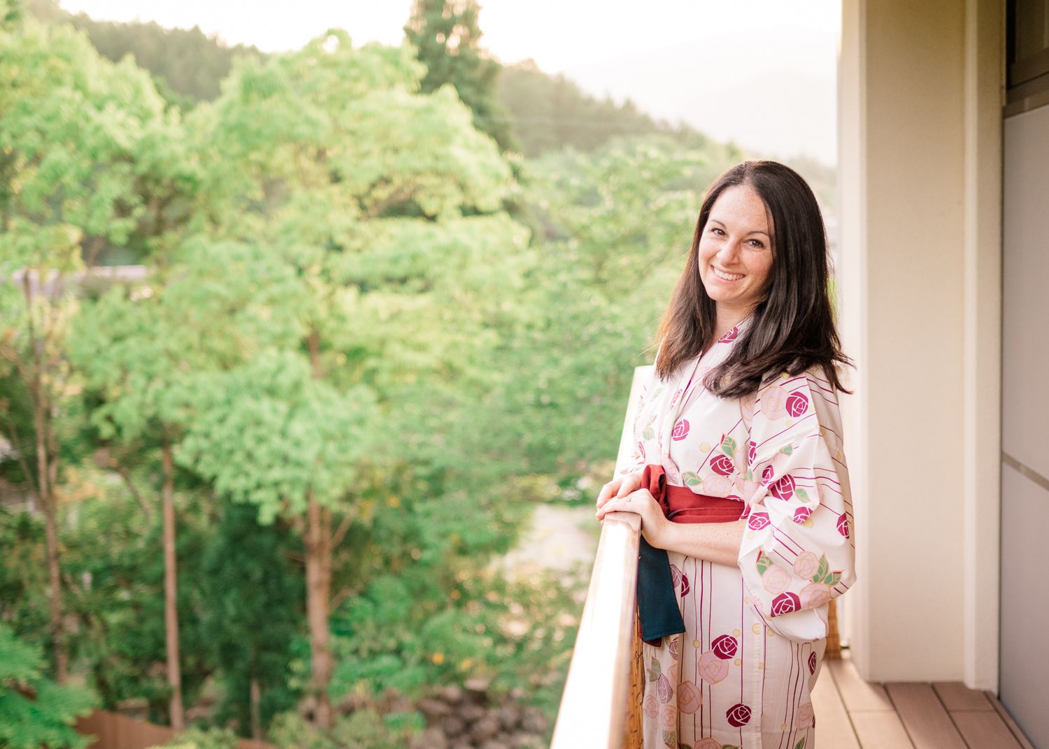 Person in floral yukata standing on balcony with forest view.