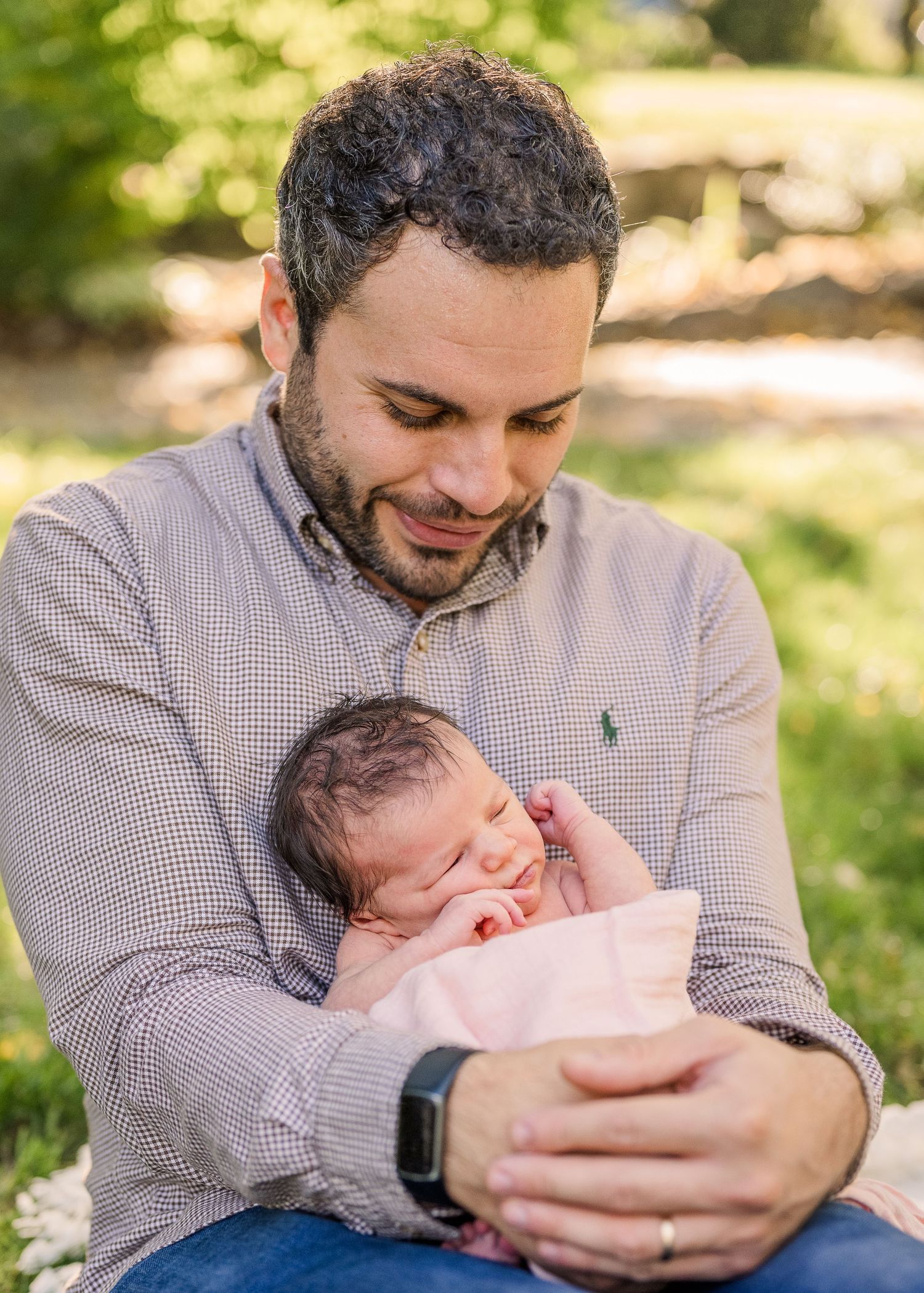 Tender moment between father and newborn baby outdoors in natural sunlight.