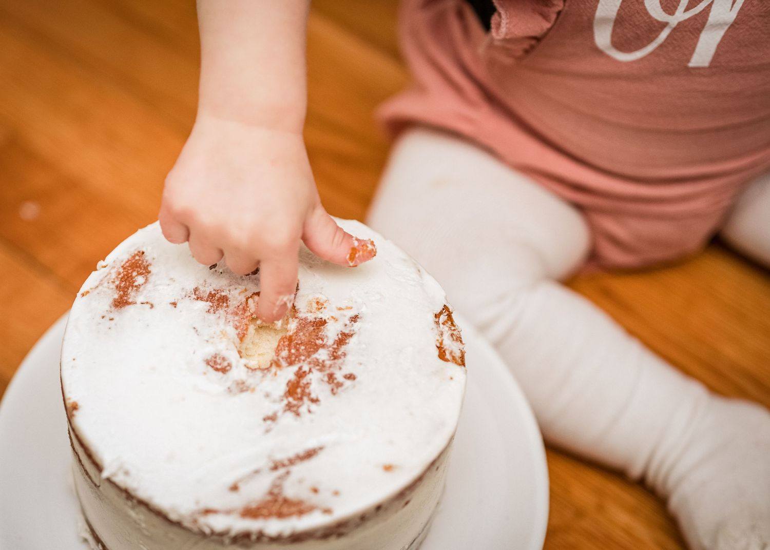 Small hands smash into a white frosted cake creating a messy celebration.