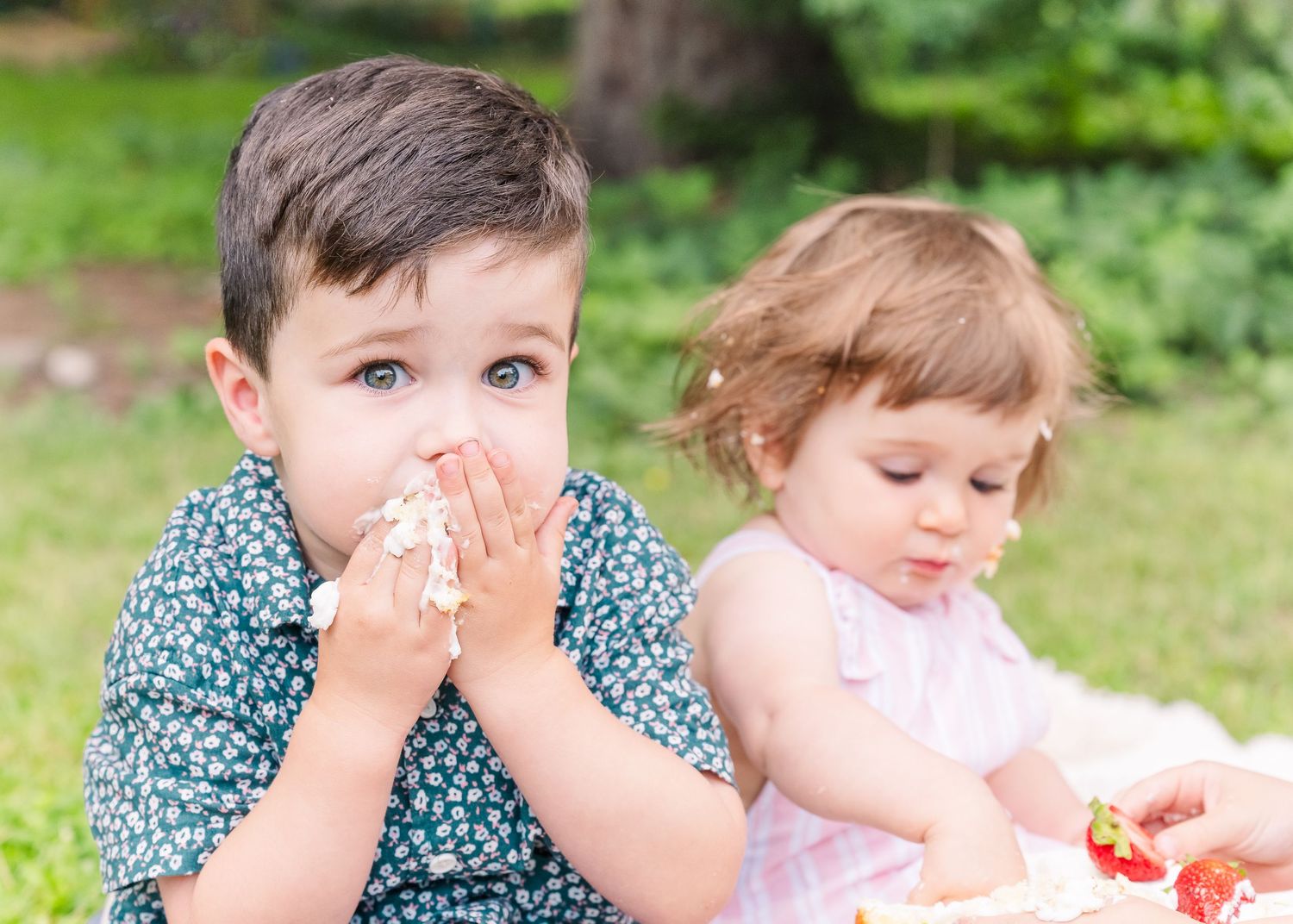 Children sitting outdoors on a blanket enjoying cake during a celebration.