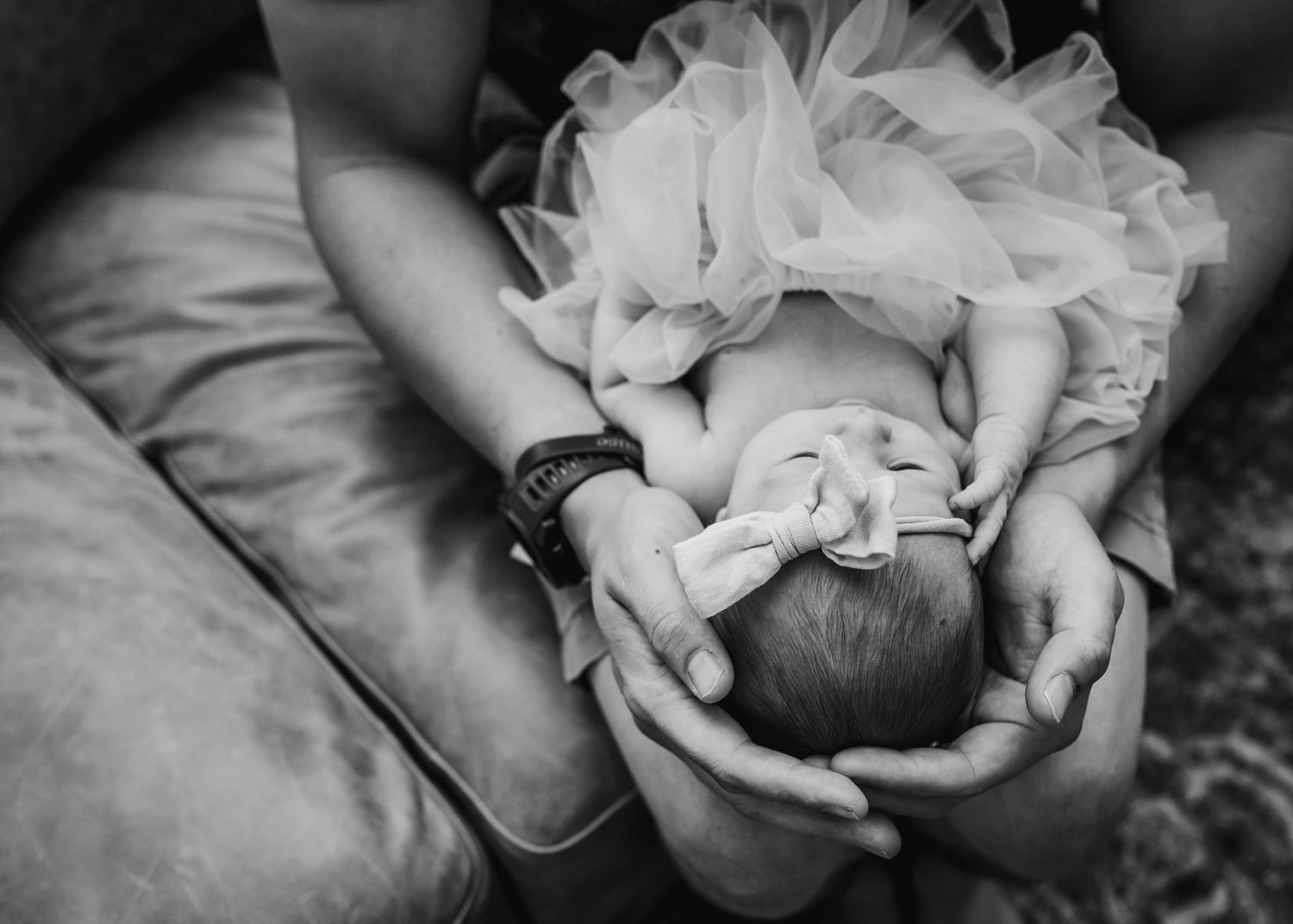 Black and white image of hands cradling newborn in tulle dress.