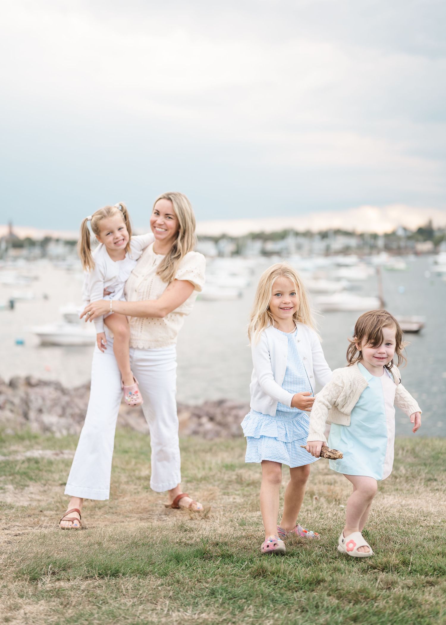 Children in white and blue outfits play together on grassy ground near a waterfront on a sunny day.