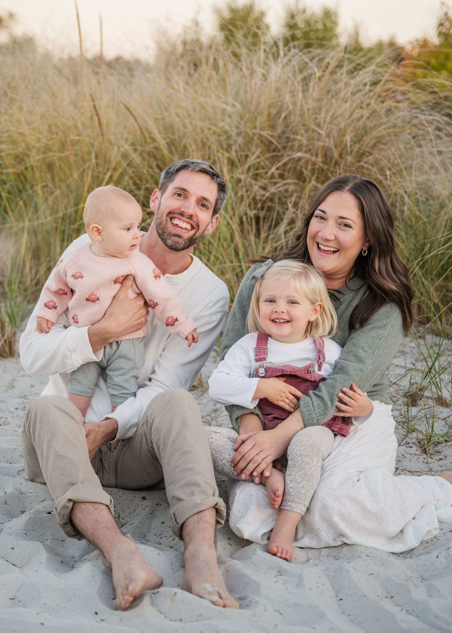 Family relaxing together on sandy beach dunes during a sunset photoshoot.