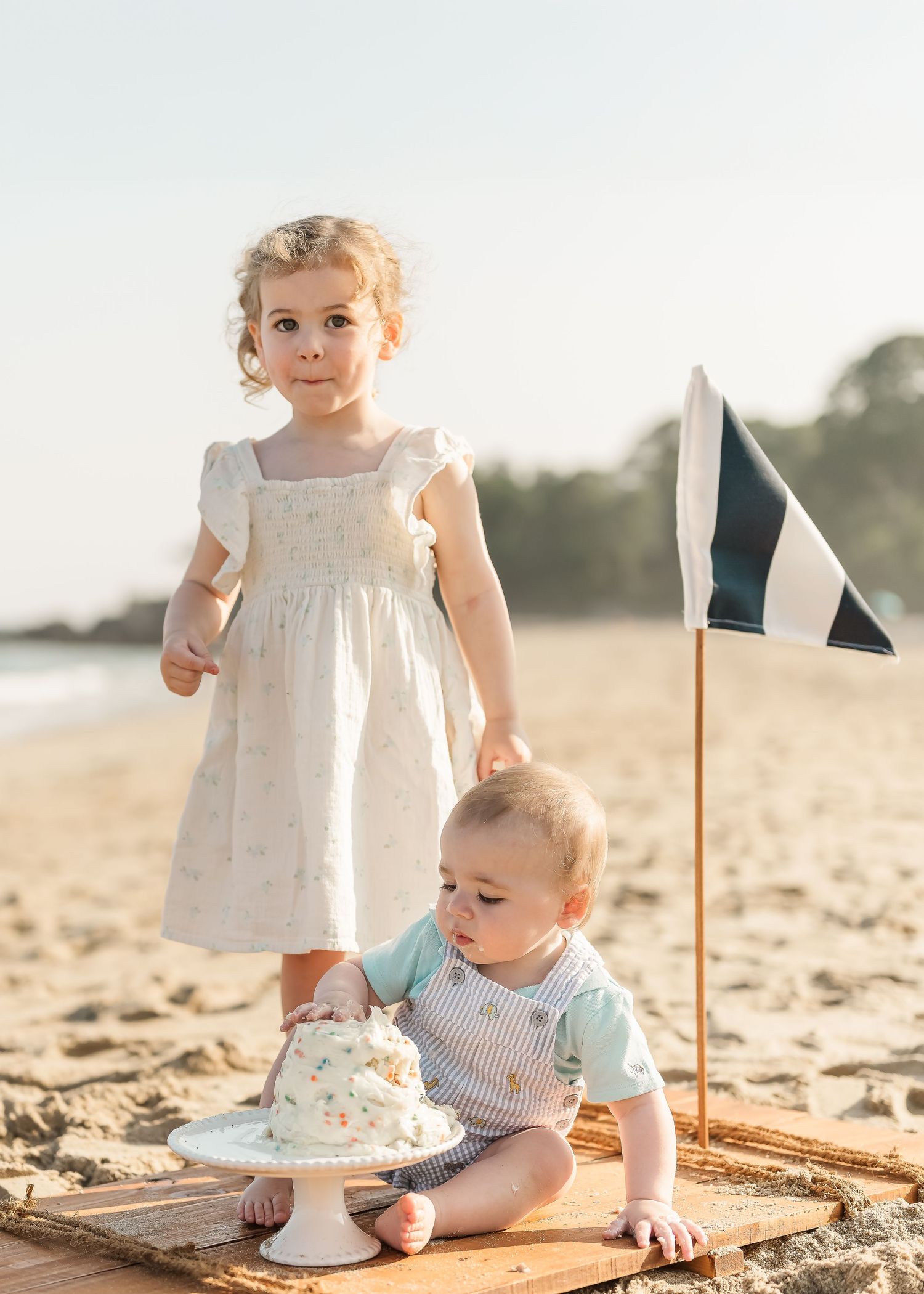 Two young children play together on a blanket at the beach during a warm sunset.