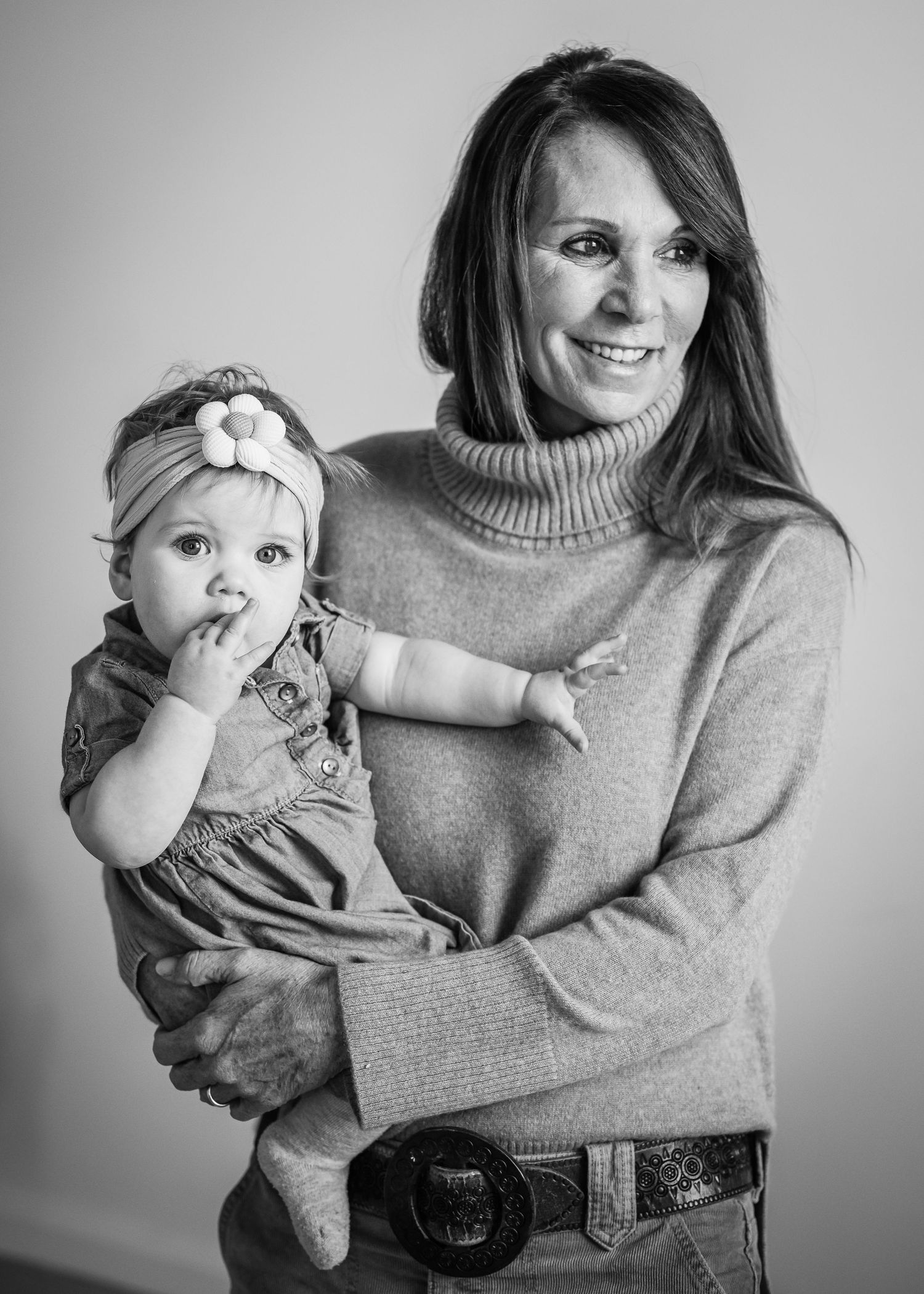 Black and white portrait of parent and baby in casual attire smiling at camera.