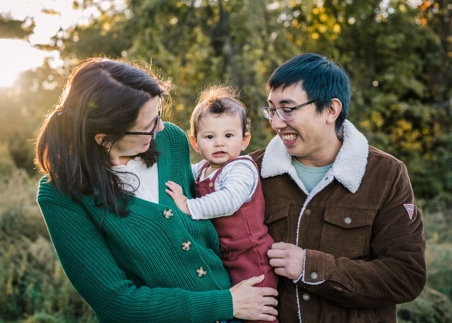 Candid outdoor family moment captured in natural lighting with green foliage background.