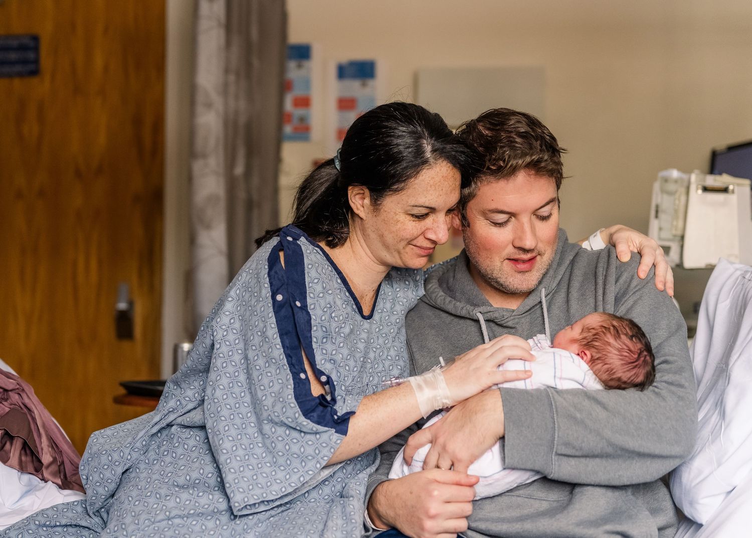 A tender moment as new parents cradle their newborn baby in a hospital room.