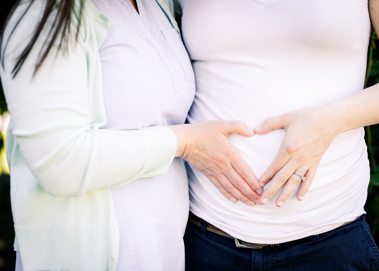 A loving maternity moment as hands form a heart shape over a pregnant belly.